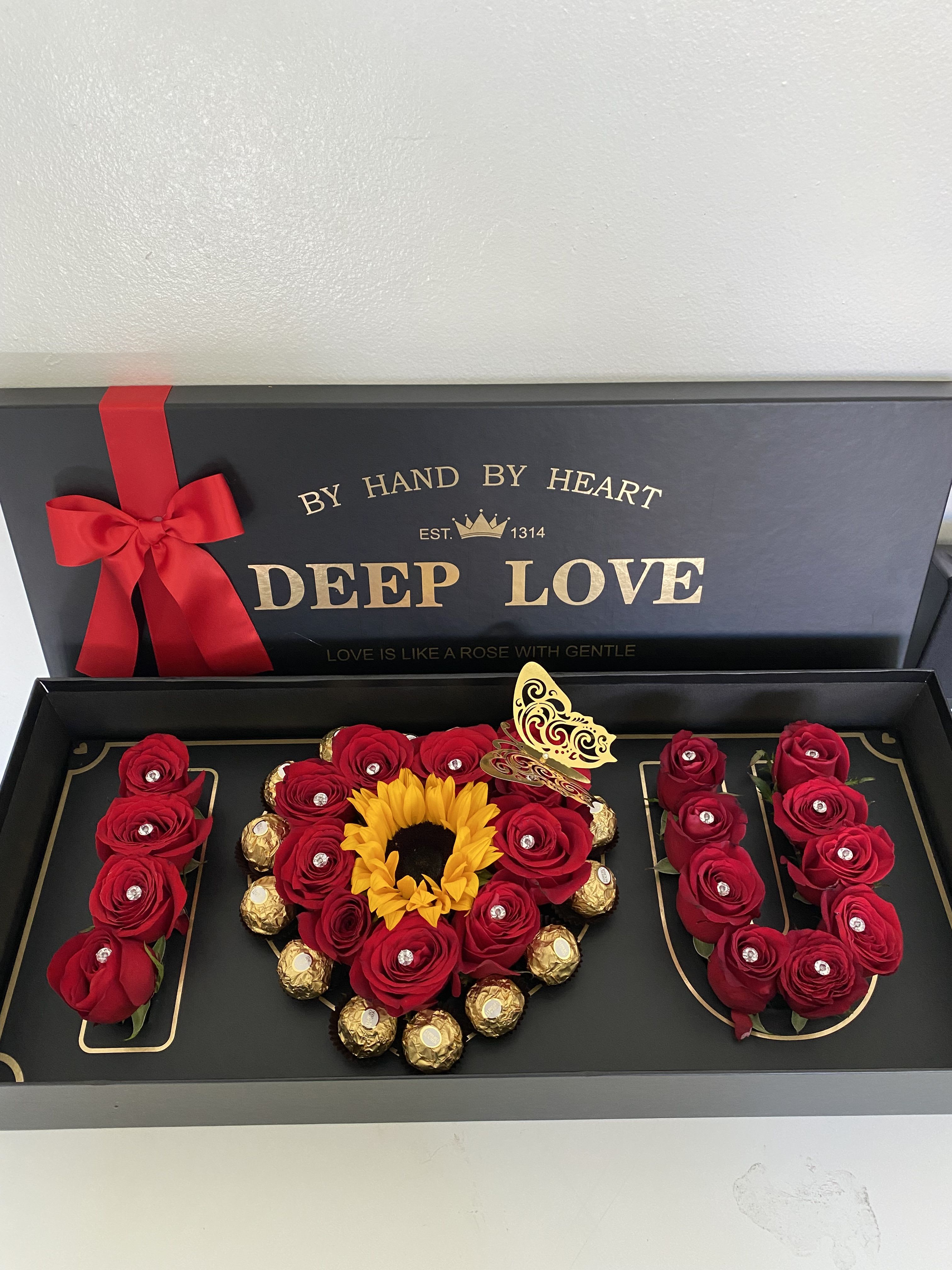 Gift box with red roses, a sunflower, and chocolates arranged in the shape of "I LOVE U"