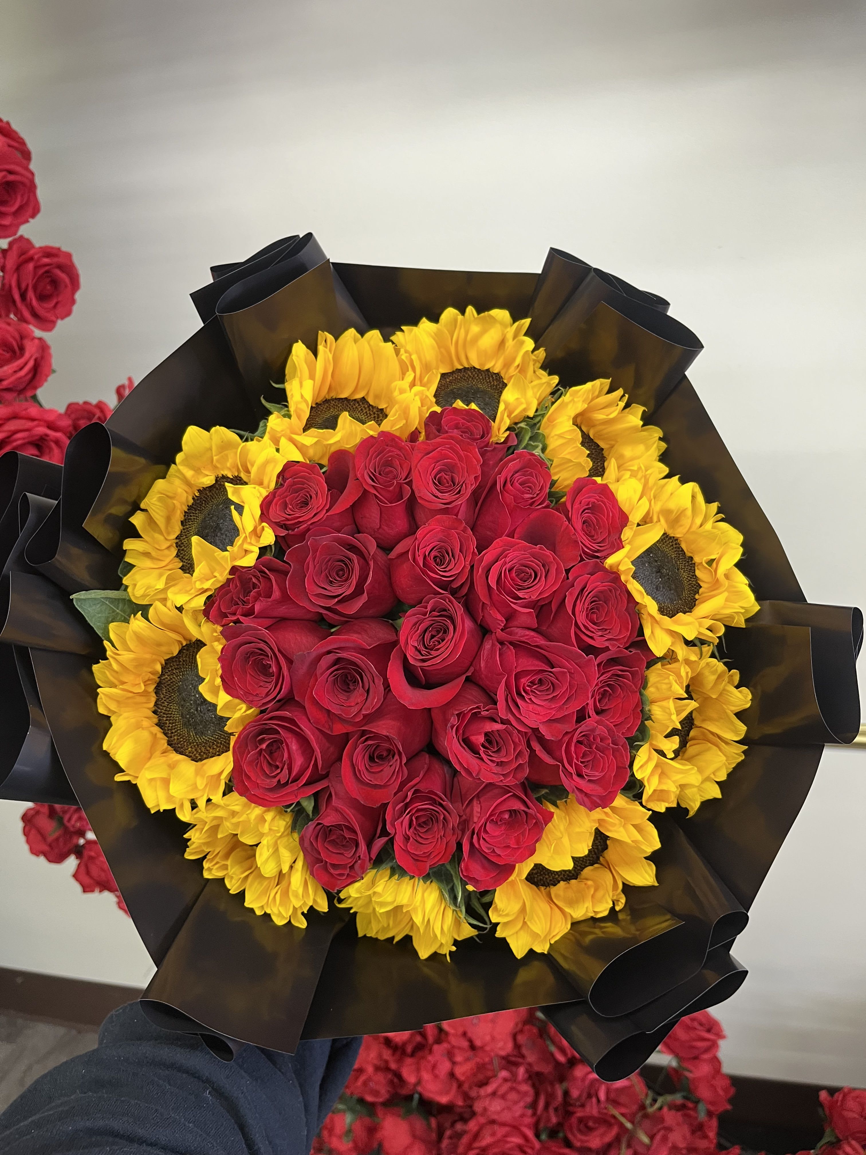 Bouquet of red roses surrounded by yellow sunflowers in black wrap