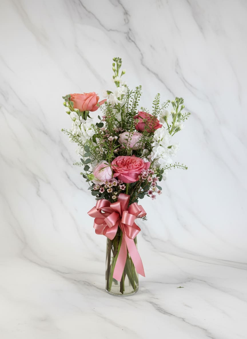 Pink and white rose bouquet in a clear glass vase with a pink ribbon