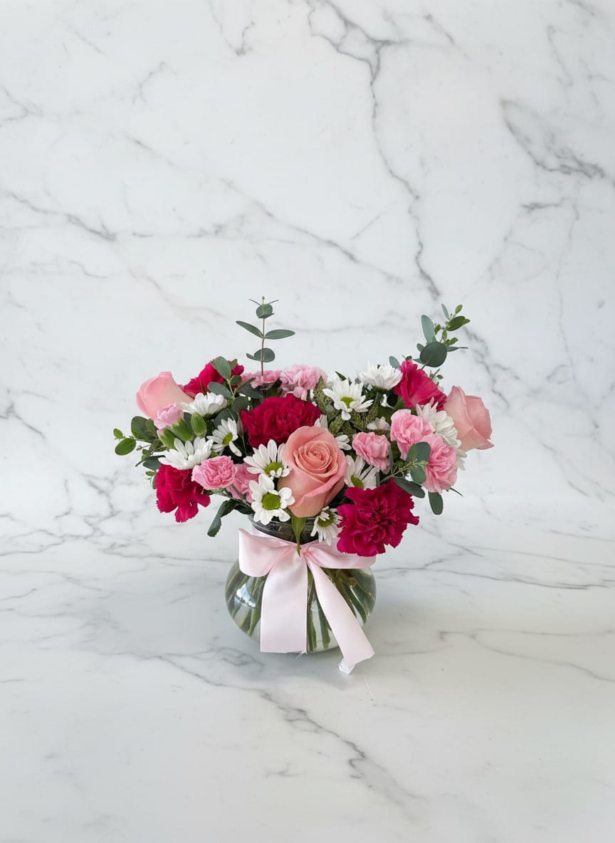 Pink and white mixed flower arrangement in a glass vase with a ribbon