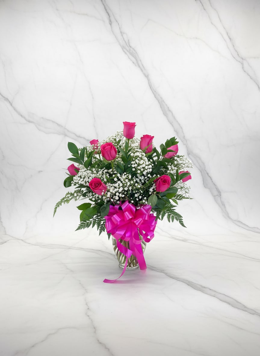 Pink roses and baby's breath in a glass vase with a magenta bow