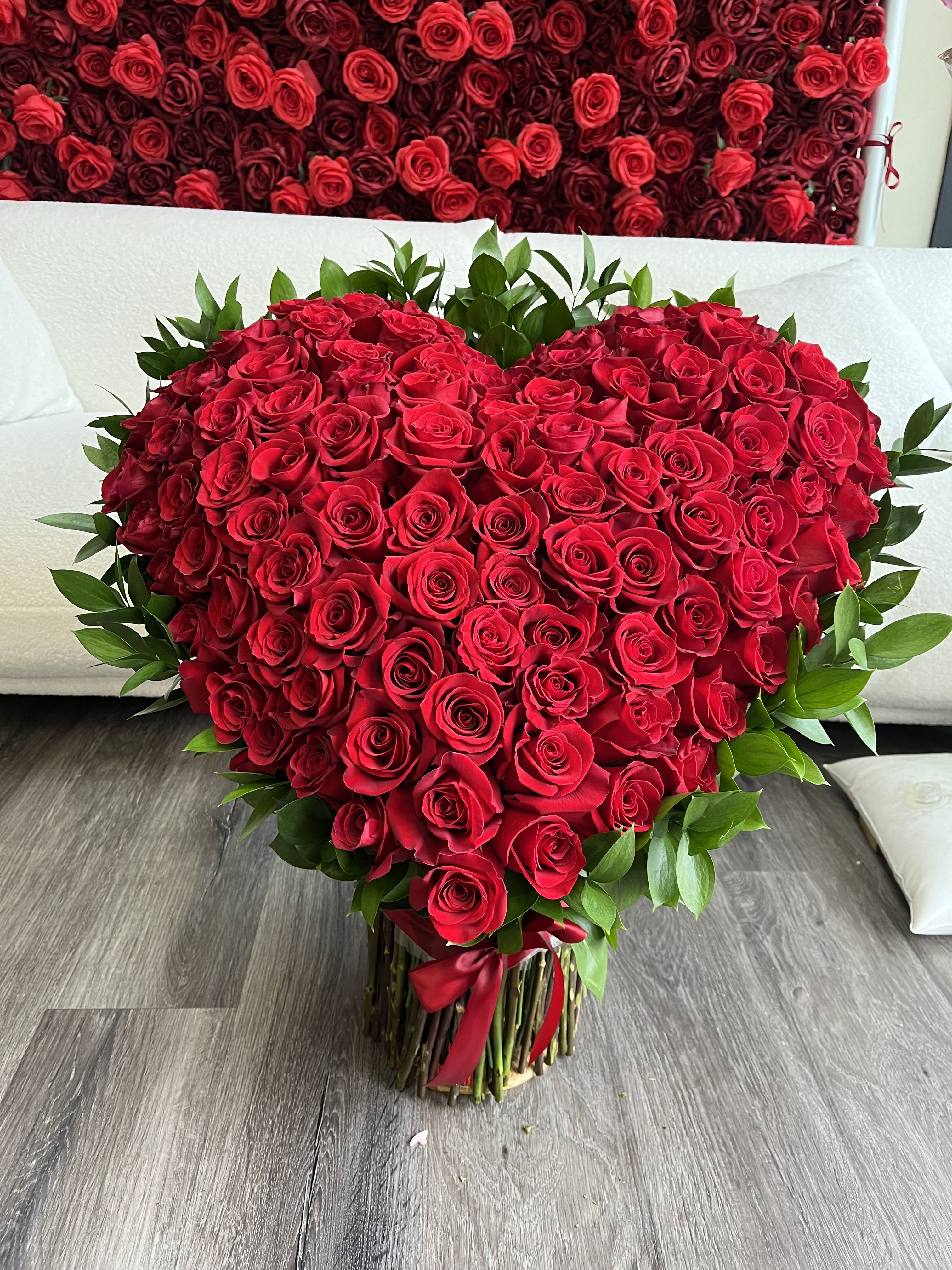 Heart-shaped bouquet of red roses with green foliage and a red ribbon