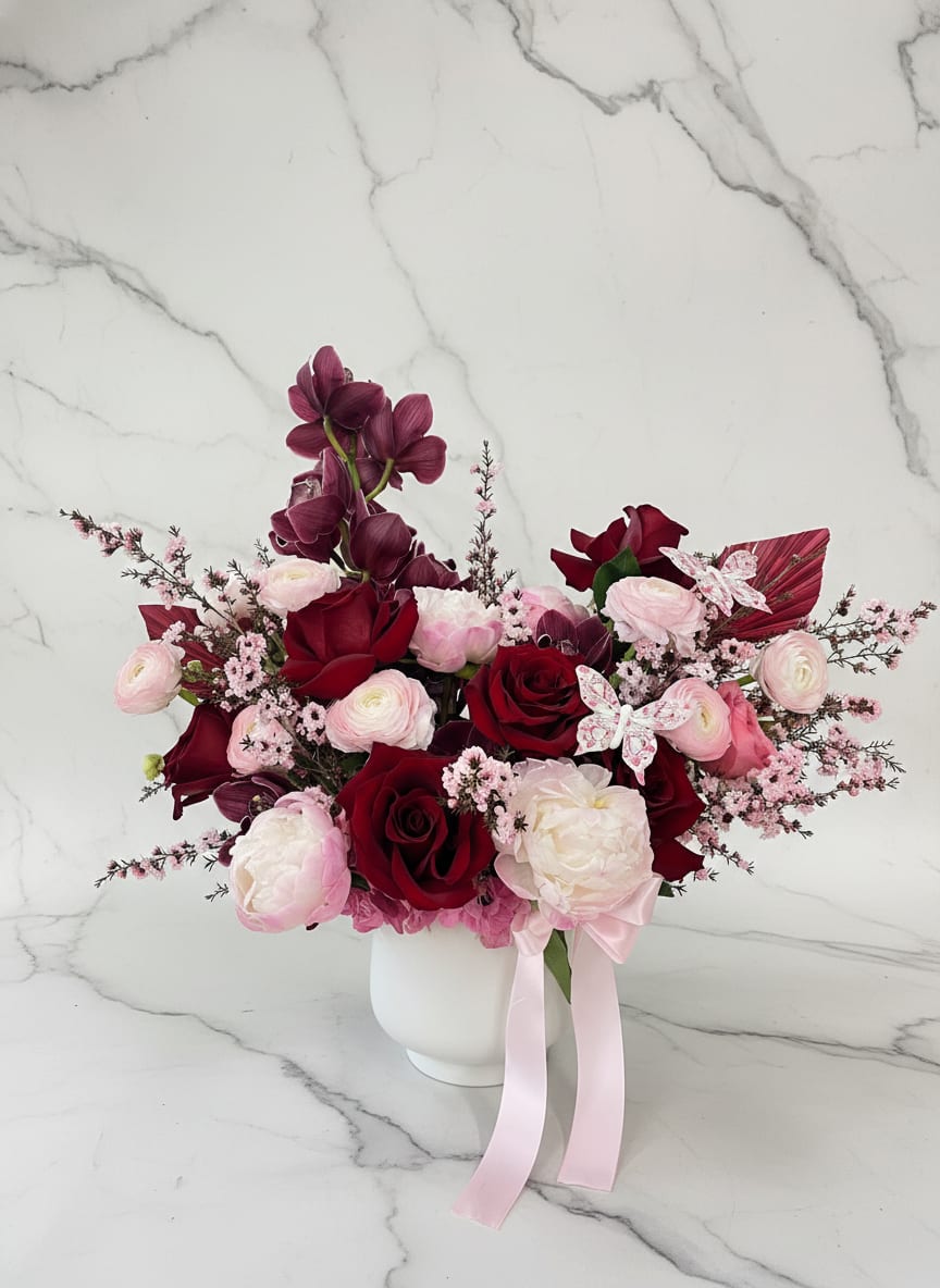 Bouquet of red and pink flowers in a white vase with a pink ribbon