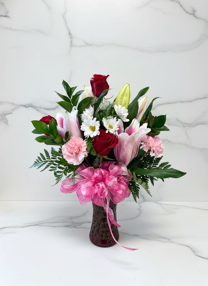 Bouquet of red roses, pink lilies, and white daisies in a vase with a pink bow