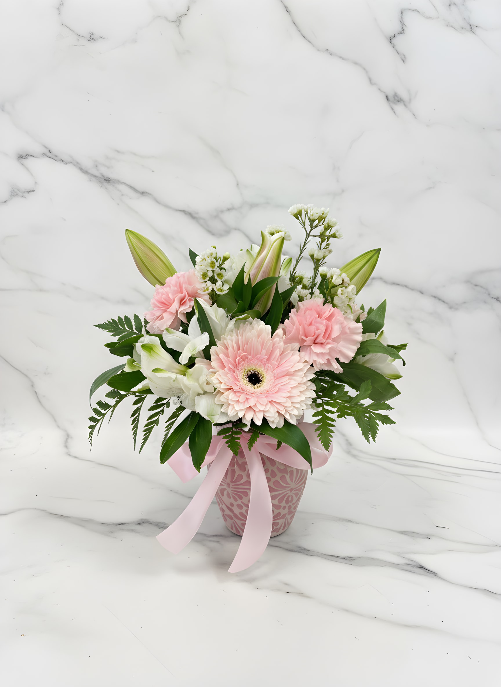Cielito Lindo Pink - A vibrant arrangement of  pink Gerbera daisy, soft light pink lilies, carnations, and delicate wax flower, beautifully styled in a colorful ceramic Mexican-inspired vase with fresh greenery.