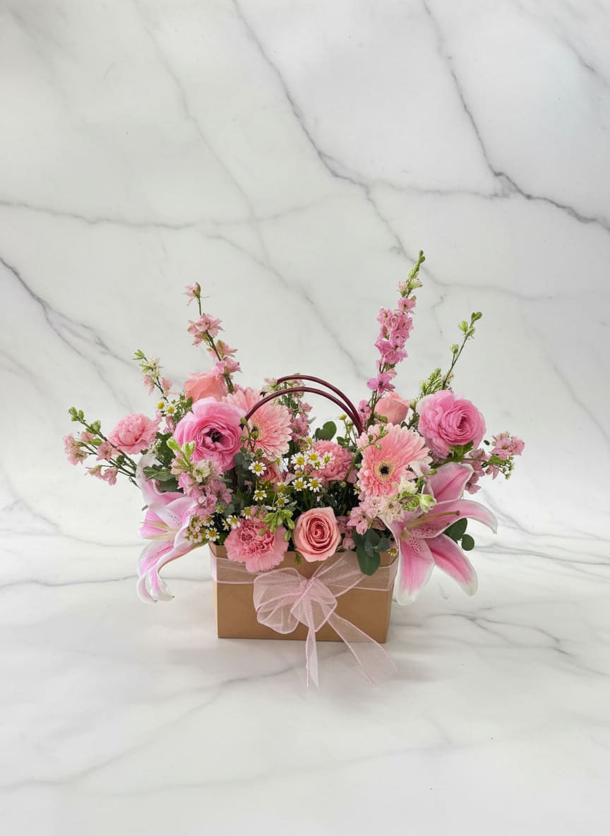 Blooming Bag  - Soft pink roses, gerberas, lilies and white daisies with green accents in a gift-ready brown box and pink ribbon-cheerful, romantic arrangement perfect for birthdays, anniversaries, or Mother's Day.