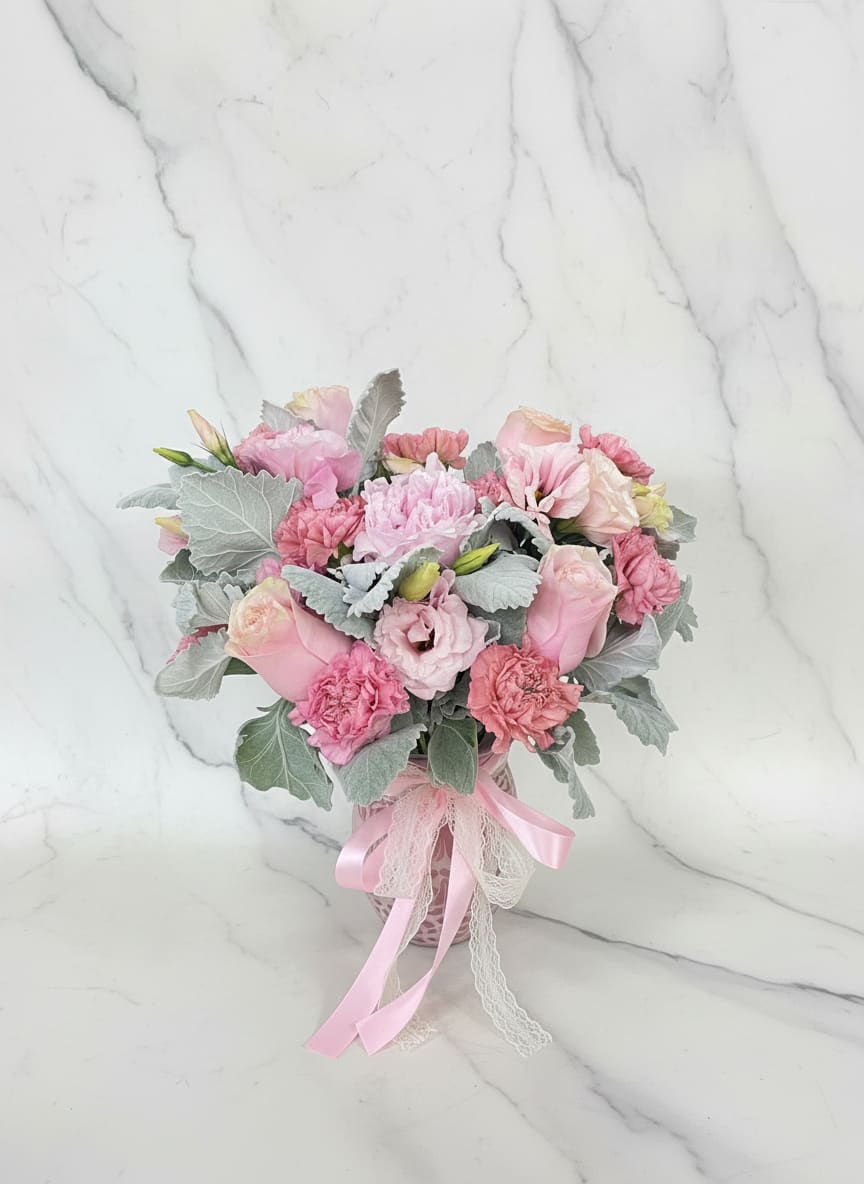 Peony Cielito Lindo Jar - Blush Pink roses, lisianthus, and carnations in a decorative pink vase with satin and lace ribbons-soft, romantic blooms with silvery foliage, perfect for Mother's Day or any special moment.