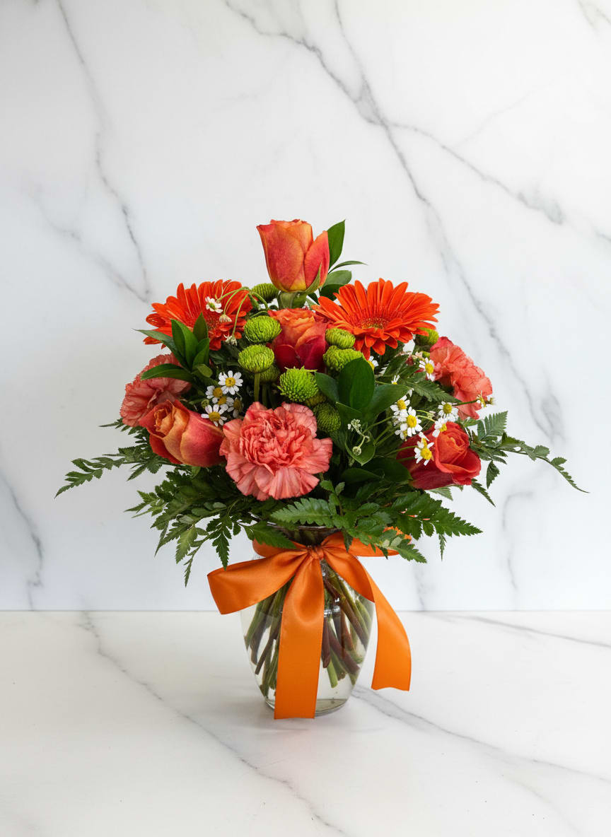 Orange and coral bouquet in a glass vase with a ribbon