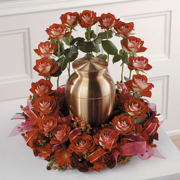 Red roses arranged around a bronze urn with pink ribbon accents