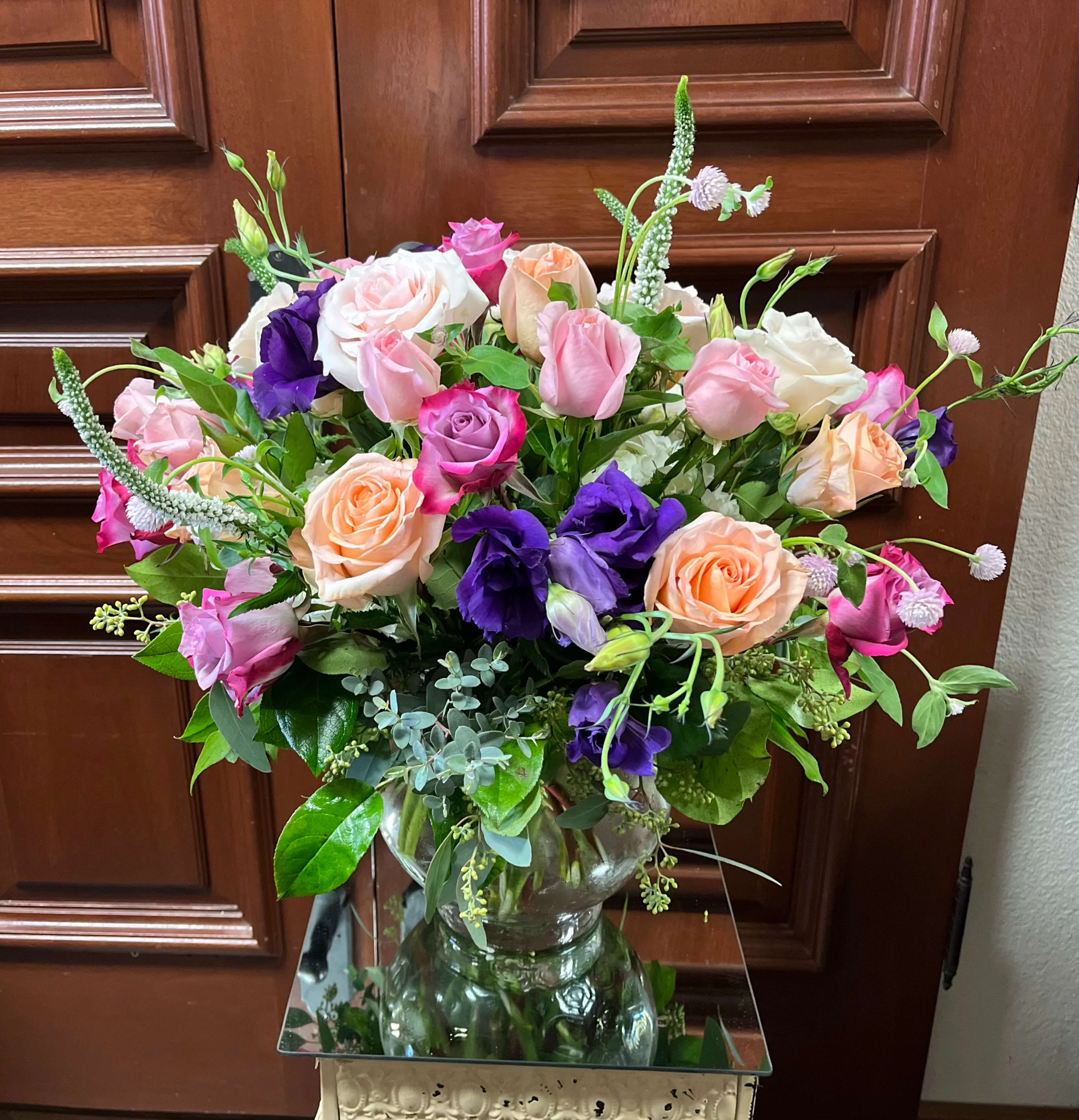 Mixed bouquet of pink, peach, white, and purple roses in a glass vase