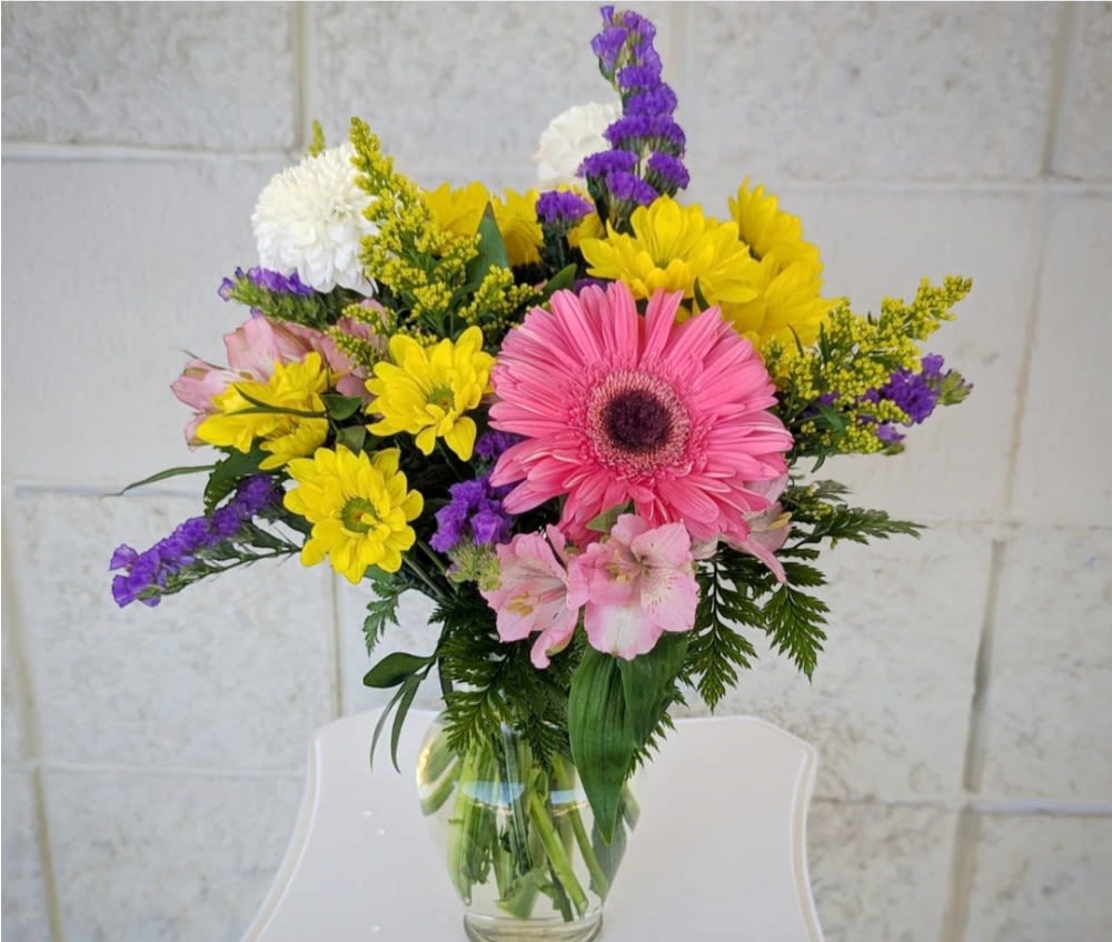 Mixed bouquet of pink, yellow, purple, and white flowers in a glass vase