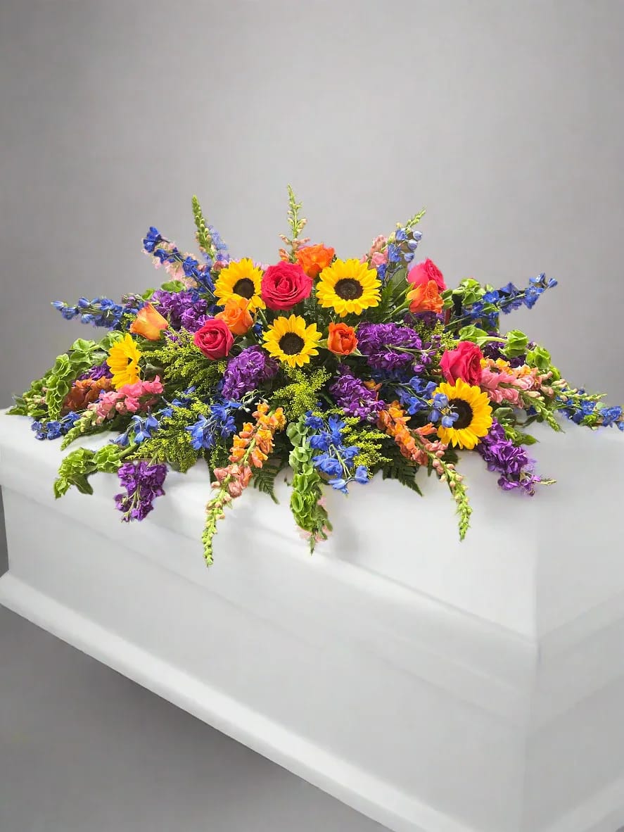 Colorful floral casket spray with sunflowers, roses, and purple blooms