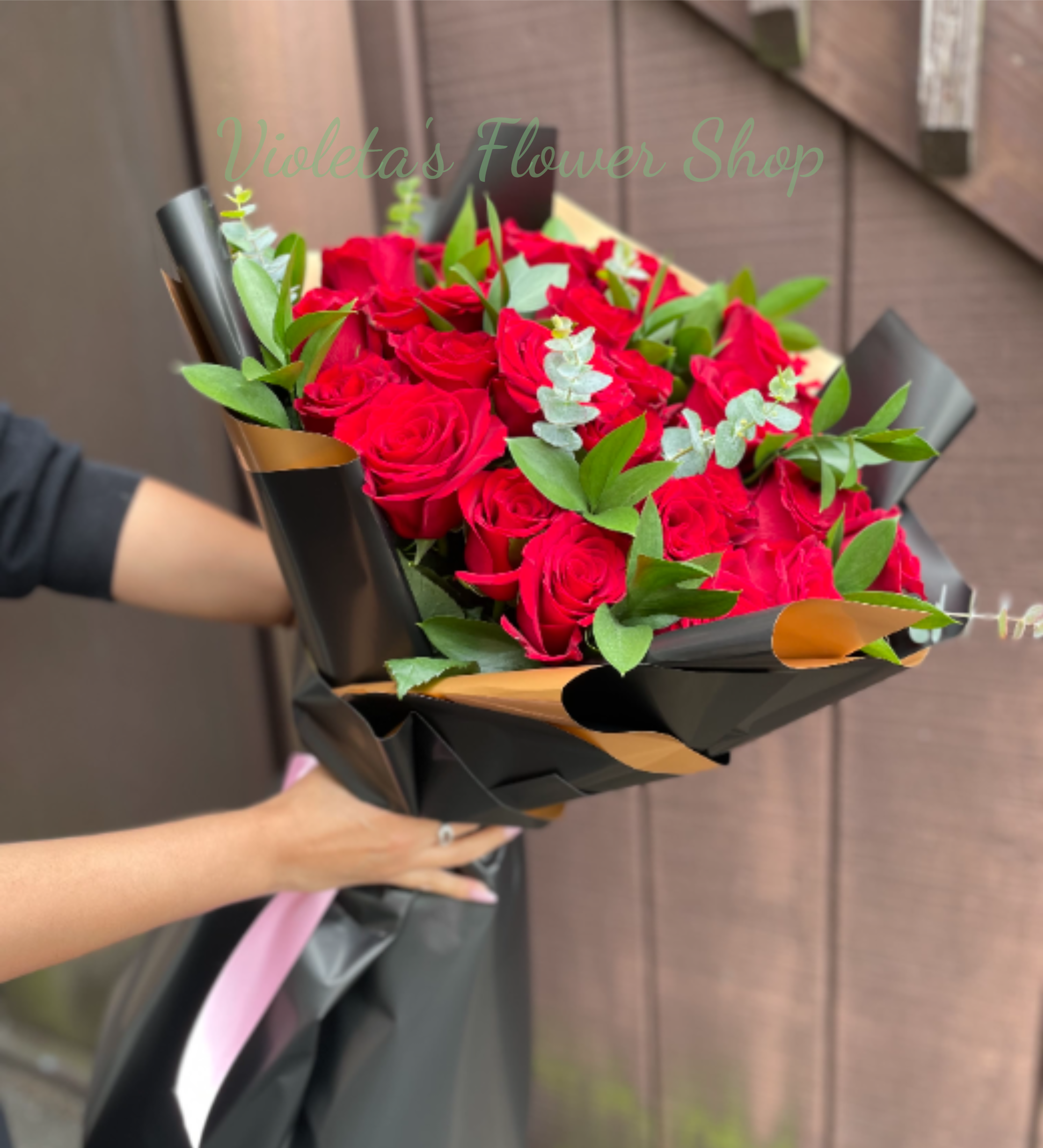 Bouquet of Explorer Roses - A dense cluster of red roses bundled in a rounded hand-tied form makes a striking romantic statement - perfect as an anniversary bouquet, Valentine's Day arrangement, or a birthday surprise for the person you're thinking of. The dramatic contrast of deep red blooms against matte black wrapping with gold-toned inner folds creates an immediately memorable visual, while the soft pink ribbon adds a tender finishing touch so she feels celebrated the moment the package is opened.  Each bouquet features long-stem red roses accented with pale eucalyptus-like sprigs for soft texture and subtle fragrance, wrapped in decorative matte black paper with gold interior panels and secured with a delicate pink ribbon. The presentation reads polished and bold; choose it when you want a classic rose bouquet with modern styling. Standard hand-tied size fits most vase openings - trim stems and change water every 2-3 days to keep the roses looking their best. This bouquet does not includes a vase.