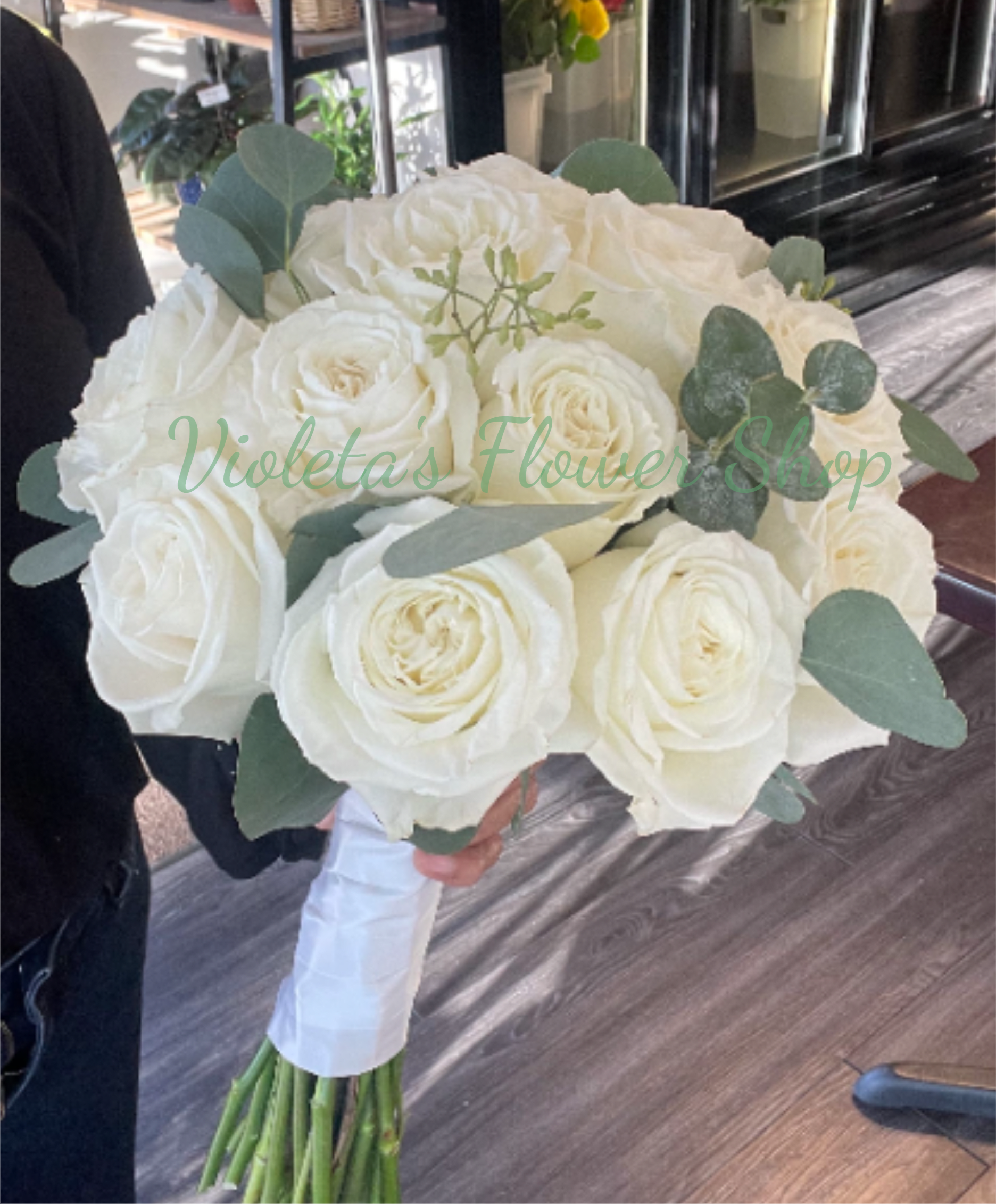 White roses and eucalyptus Bouquet - A lush cluster of large white roses arranged in a classic rounded bridal shape-this white roses and eucalyptus bouquet makes a timeless statement for weddings and bridal bouquets. The clean white blooms read as pure and romantic, while the muted blue‑green eucalyptus tucked between the roses adds cool contrast and soft texture that will make the person you're celebrating look radiant at the altar.  The bouquet is tightly packed for a full, formal silhouette with eucalyptus accents woven throughout to keep the look fresh and modern. Stems are finished with white ribbon wrap and a bouquet wrap for a polished, easy-to-hold presentation that complements white dresses and neutral palettes. Colors: white roses with green/blue‑green foliage.  Perfect for brides, bridesmaids, or as a refined arrangement for wedding vows and rehearsal dinners-she'll feel seen and celebrated carrying this elegant bouquet. Ordering note: stems are wrapped in white ribbon for a secure, wedding-ready hold; please indicate any ribbon or stem-length preferences at checkout if you need a custom finish.