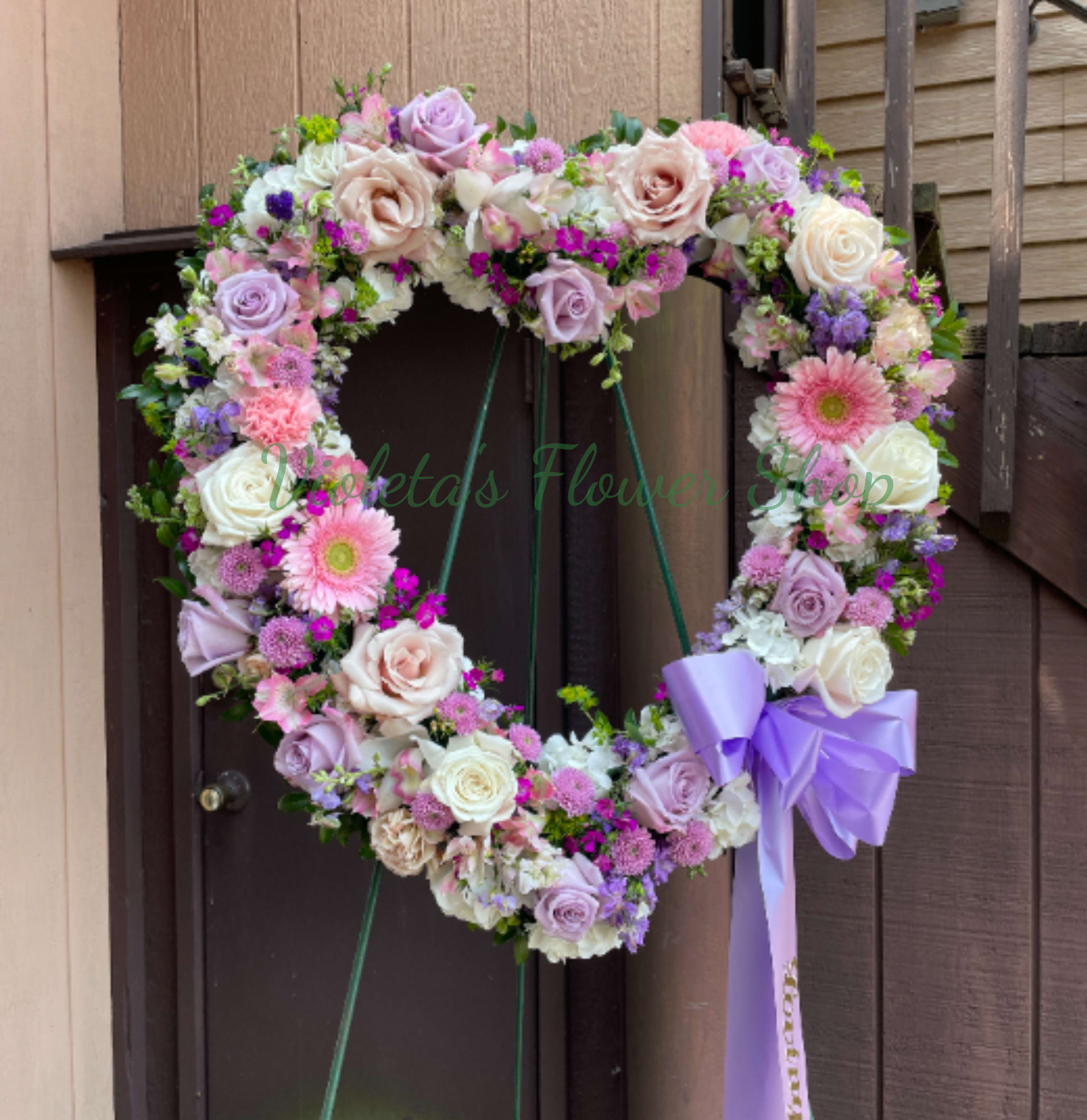 Heart-shaped floral wreath with pastel roses and gerbera daisies, tied with a lavender bow