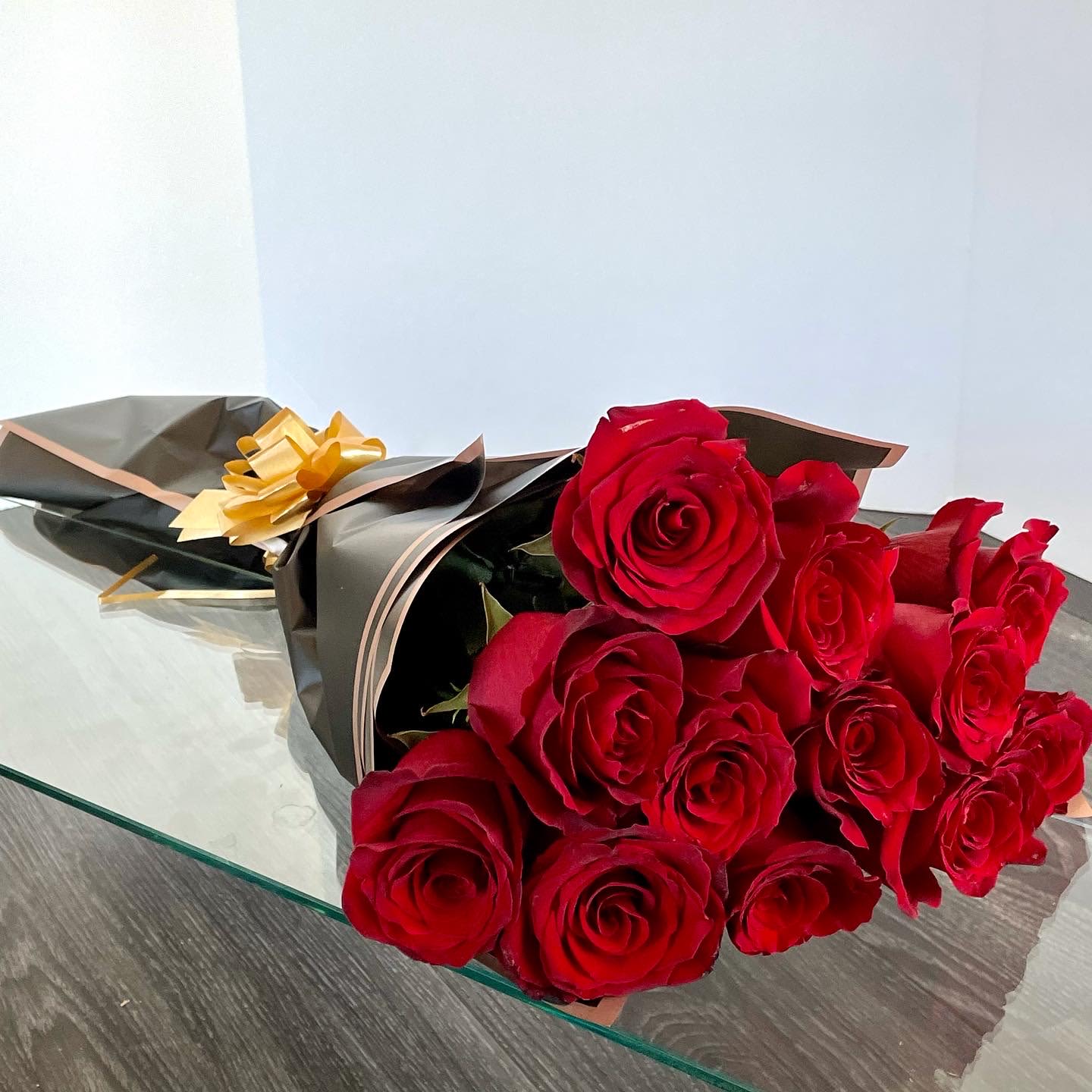 Classic Red Roses Bouquet. - A compact hand-tied bouquet of deep red roses wrapped in matte black paper with a metallic gold ribbon bow - an elegant, dramatic choice for an anniversary or Valentine's Day bouquet. The rich, velvety red of the roses pops against the dark charcoal wrapping, giving the recipient a feeling of being deeply treasured and celebrated.  This medium-sized arrangement is densely packed into a rounded, polished presentation that arrives gift-ready; decorative wrapping paper emphasize the luxurious contrast of black and gold. The tactile mix of soft rose petals, smooth matte paper, and gleaming gold ribbon creates a memorable unboxing moment.  Perfect for romantic milestones, a heartfelt "I love you," or anyone who appreciates bold, classic styling - she'll feel truly seen when handed this bouquet. Order now for hand-delivery or pickup; for best enjoyment, recut stems and place in fresh water to keep the roses looking their richest for days.