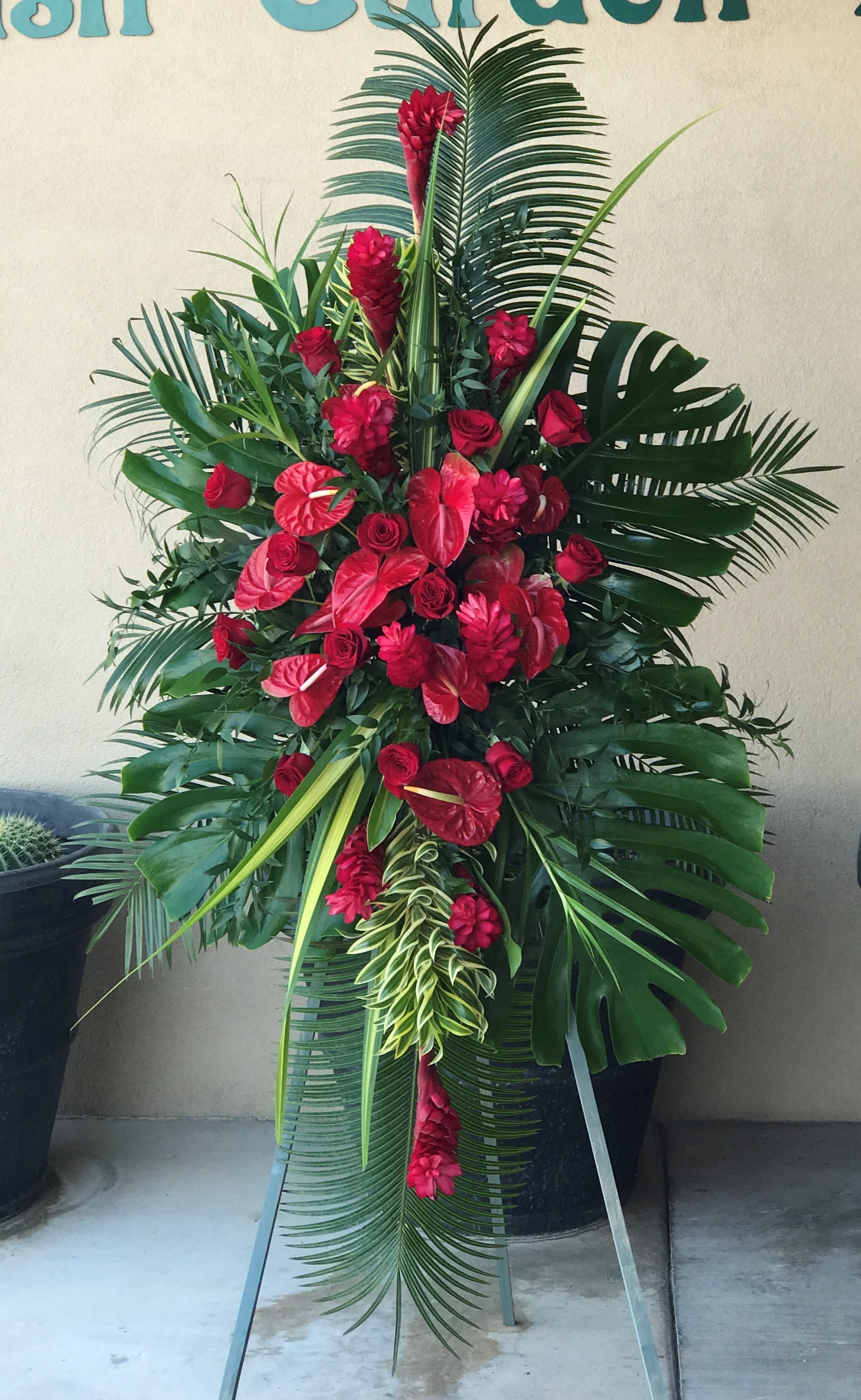 Tall red floral standing spray with tropical leaves on an easel