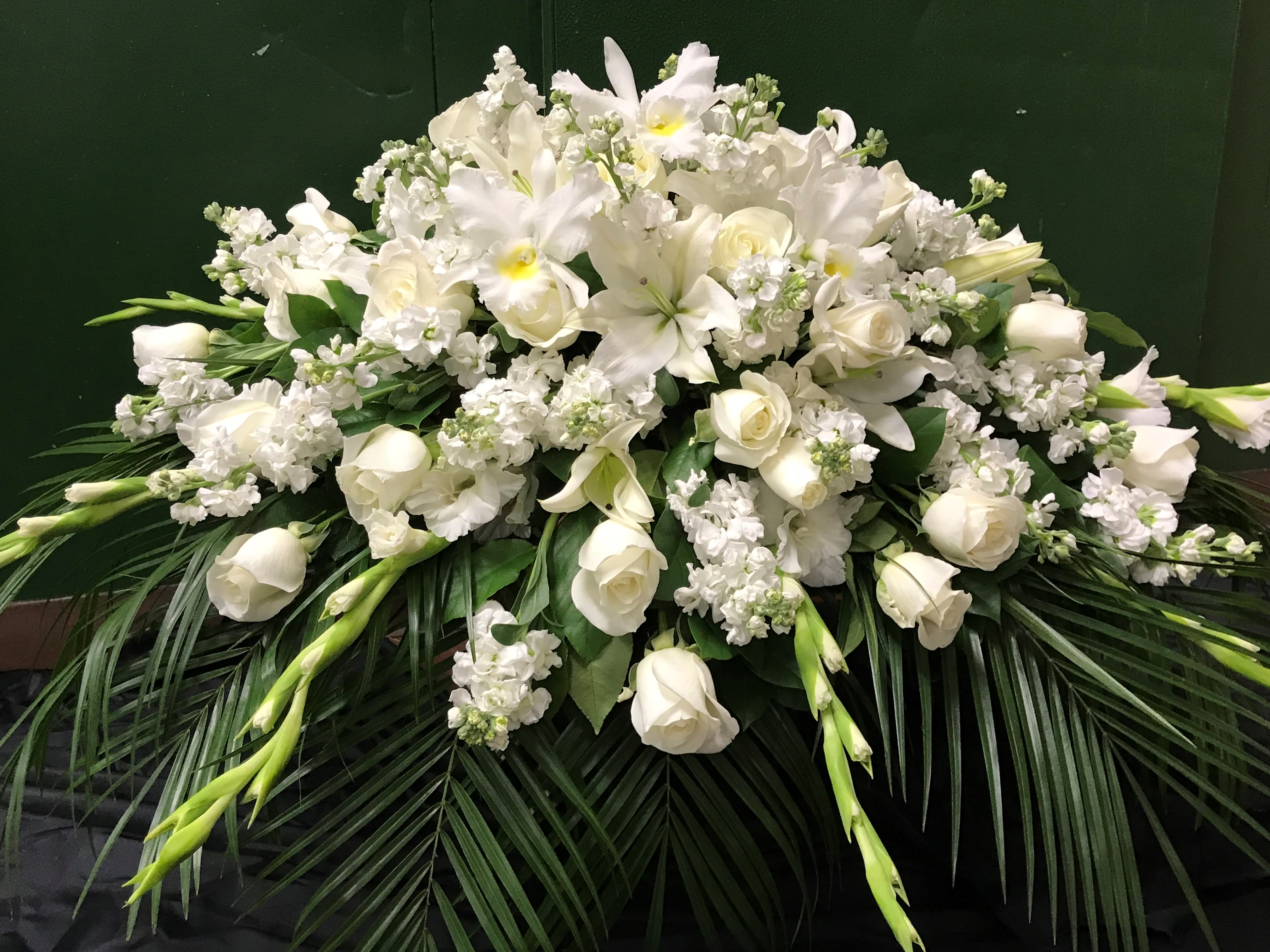 White floral casket spray with lilies, roses, and orchids