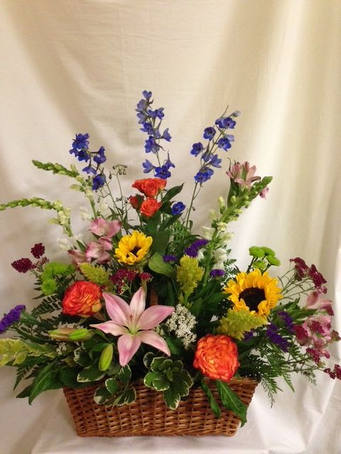 Mixed flower arrangement in a wicker basket with sunflowers, lilies, and roses