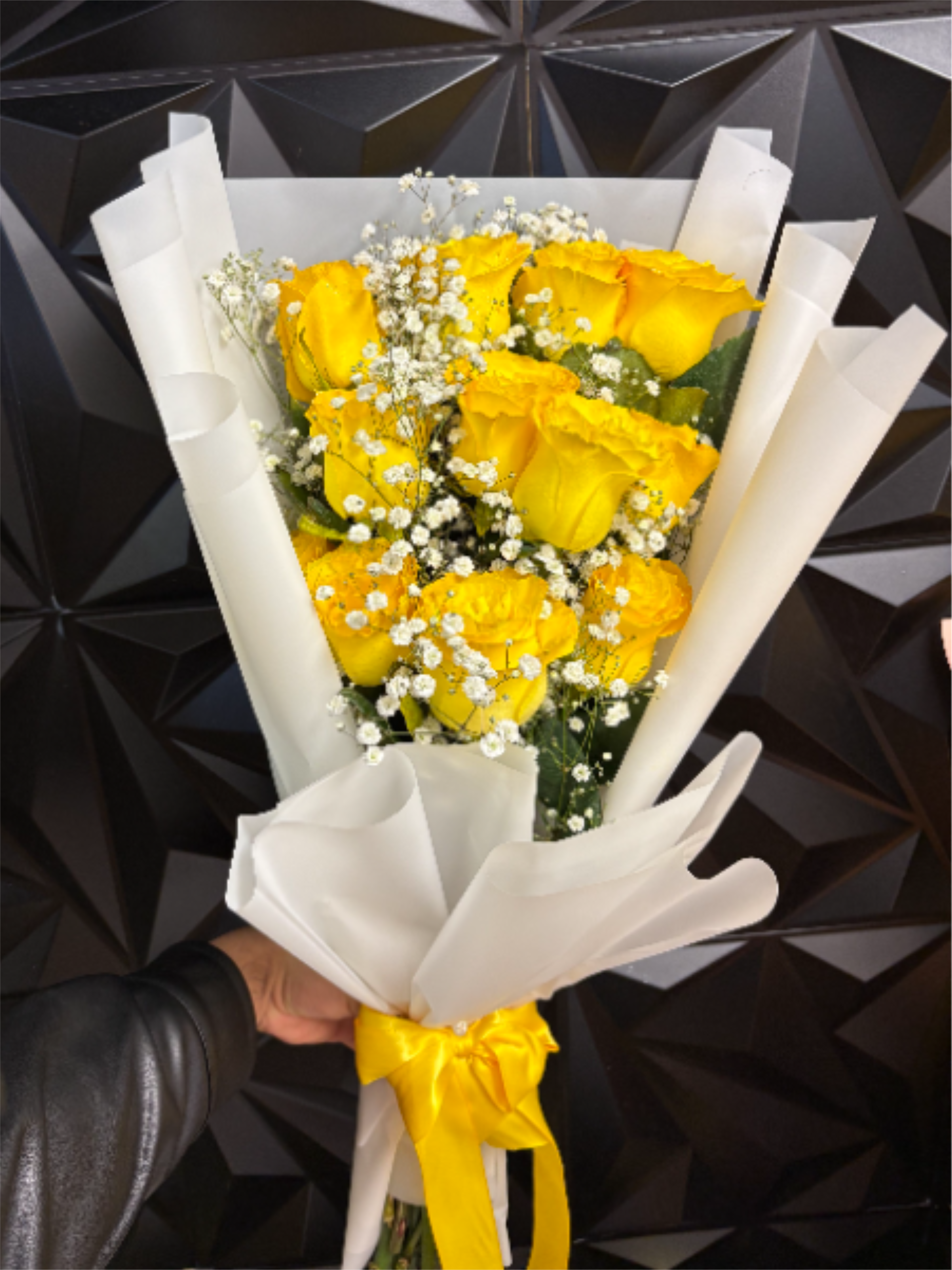 Bouquet of yellow roses with white filler flowers wrapped in white paper and tied with a yellow ribbon