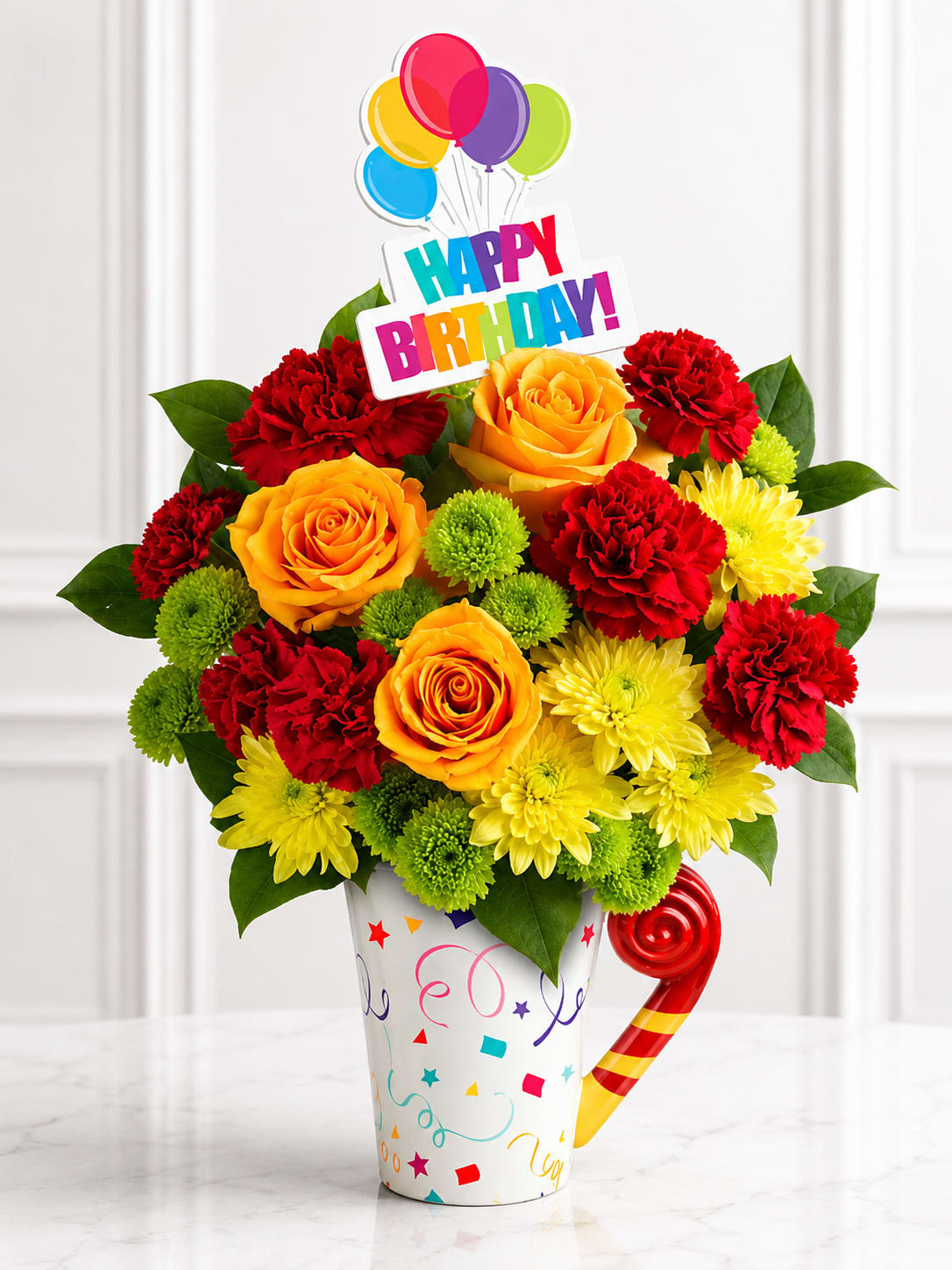 Birthday Celebration Mug™ - Make someone's birthday extra special with the Birthday Celebration Mug™, a cheerful arrangement designed in a festive keepsake birthday mug. This colorful design features vibrant orange roses, rich red carnations, sunny yellow daisies, green button poms, and fresh seasonal greenery, topped with a fun "Happy Birthday!" balloon pick. It's the perfect gift to brighten their day and create lasting memories.