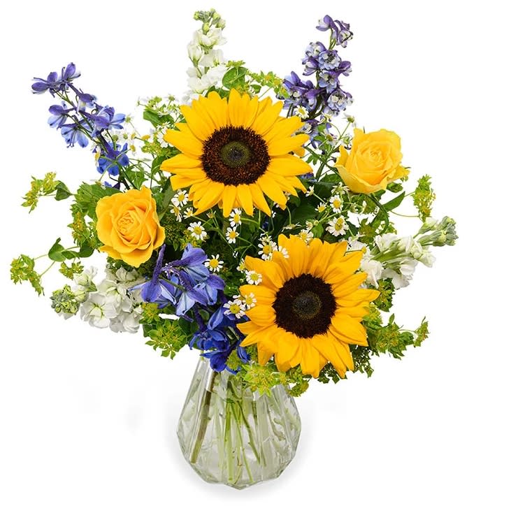 Sunflowers, yellow roses, and blue flowers in a glass vase