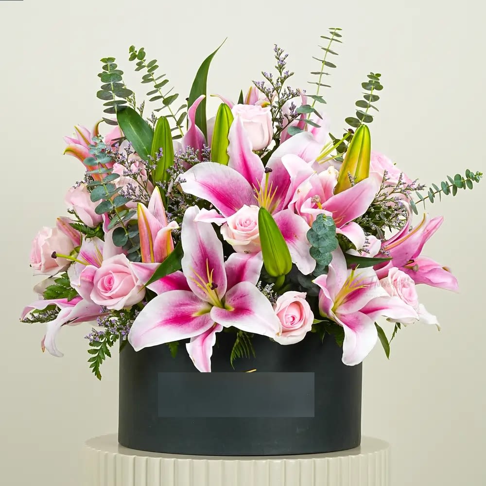 Pink lilies and roses arranged in a black box.