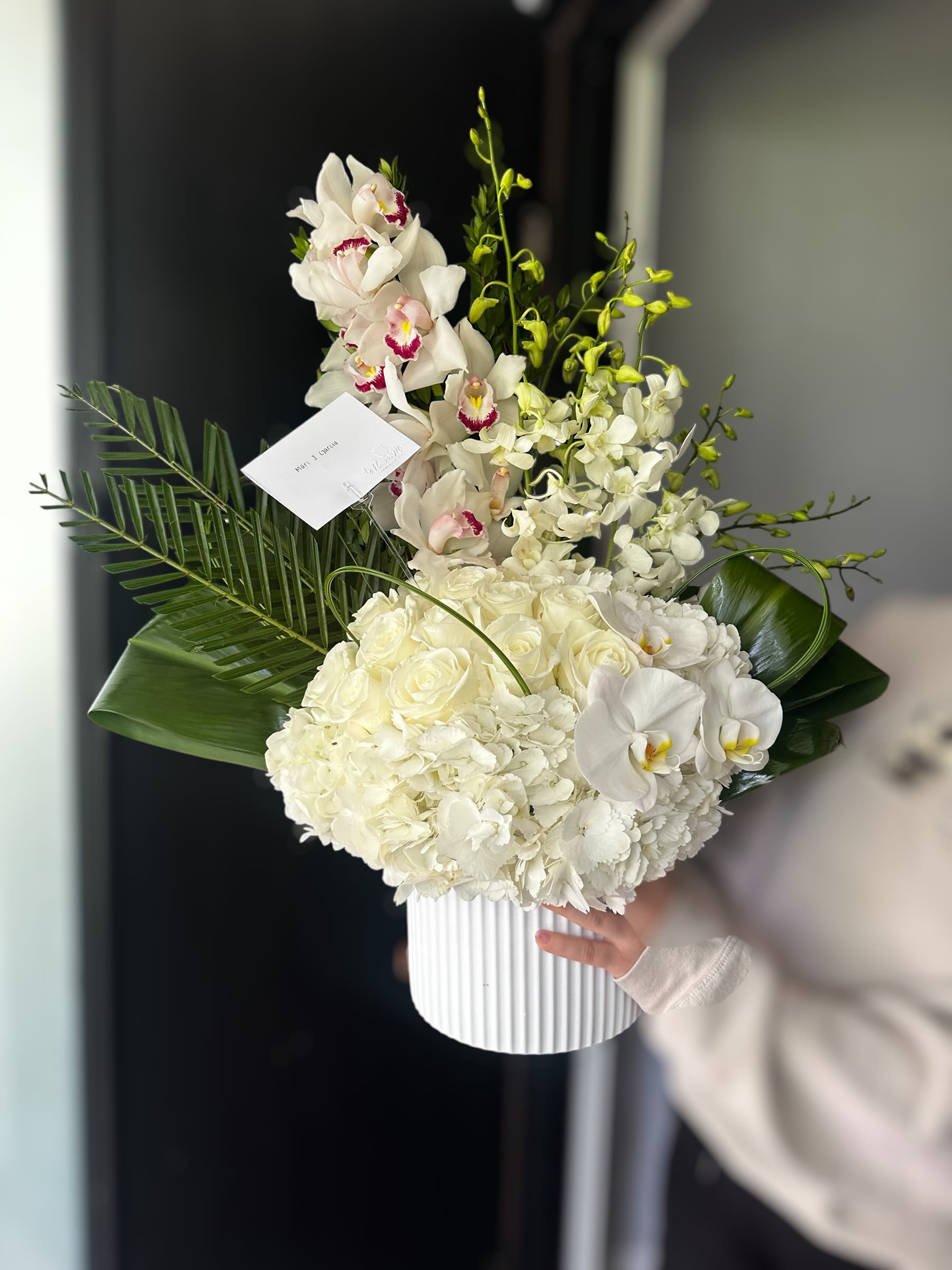 Simply Elegant - White phalaenopsis orchids, cream roses and lush hydrangeas with pink accents and green foliage in a ribbed white vase-an elegant, vertical arrangement for weddings or memorials.
