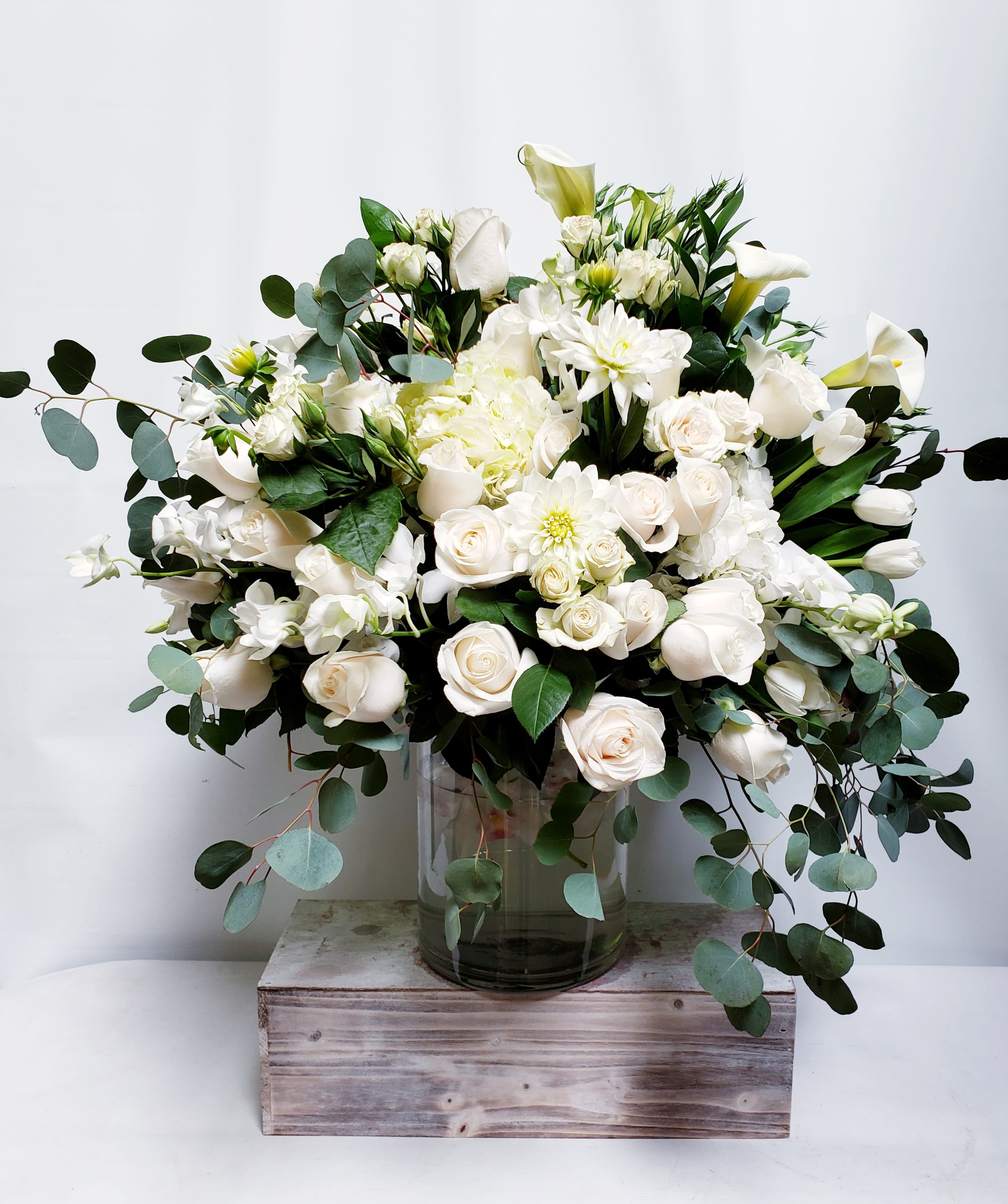 White floral arrangement in a glass vase with trailing greenery