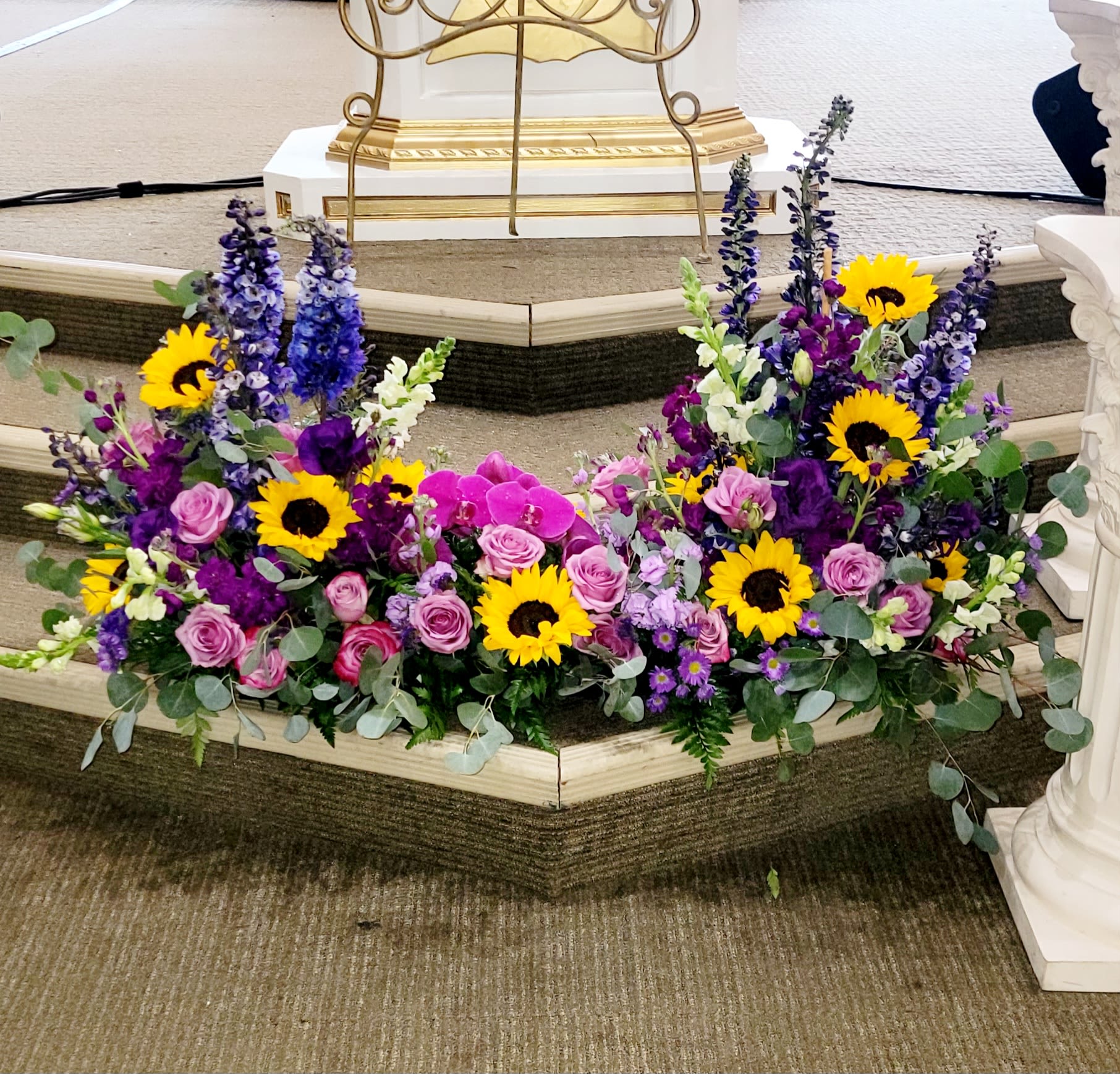 Two floral sprays with sunflowers, pink roses, and purple blooms on a church step