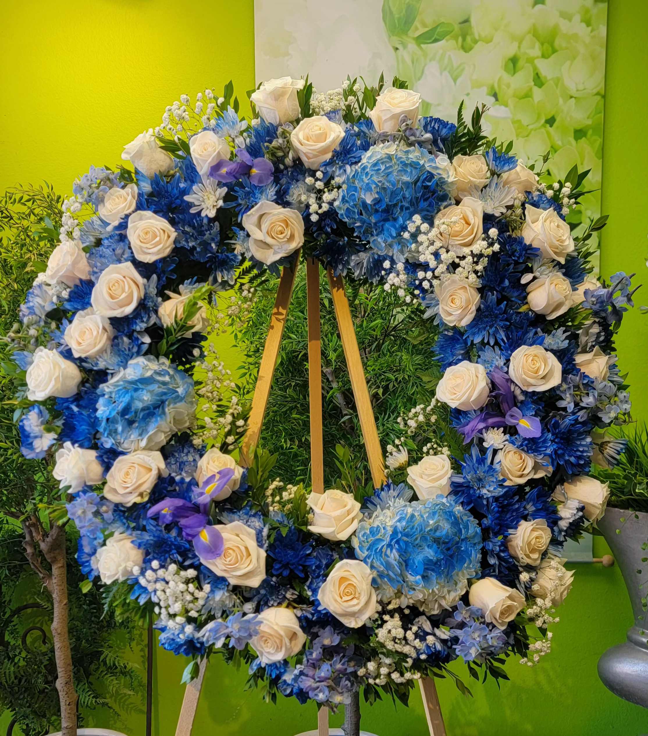 Large heart-shaped floral wreath with white roses and blue flowers on an easel