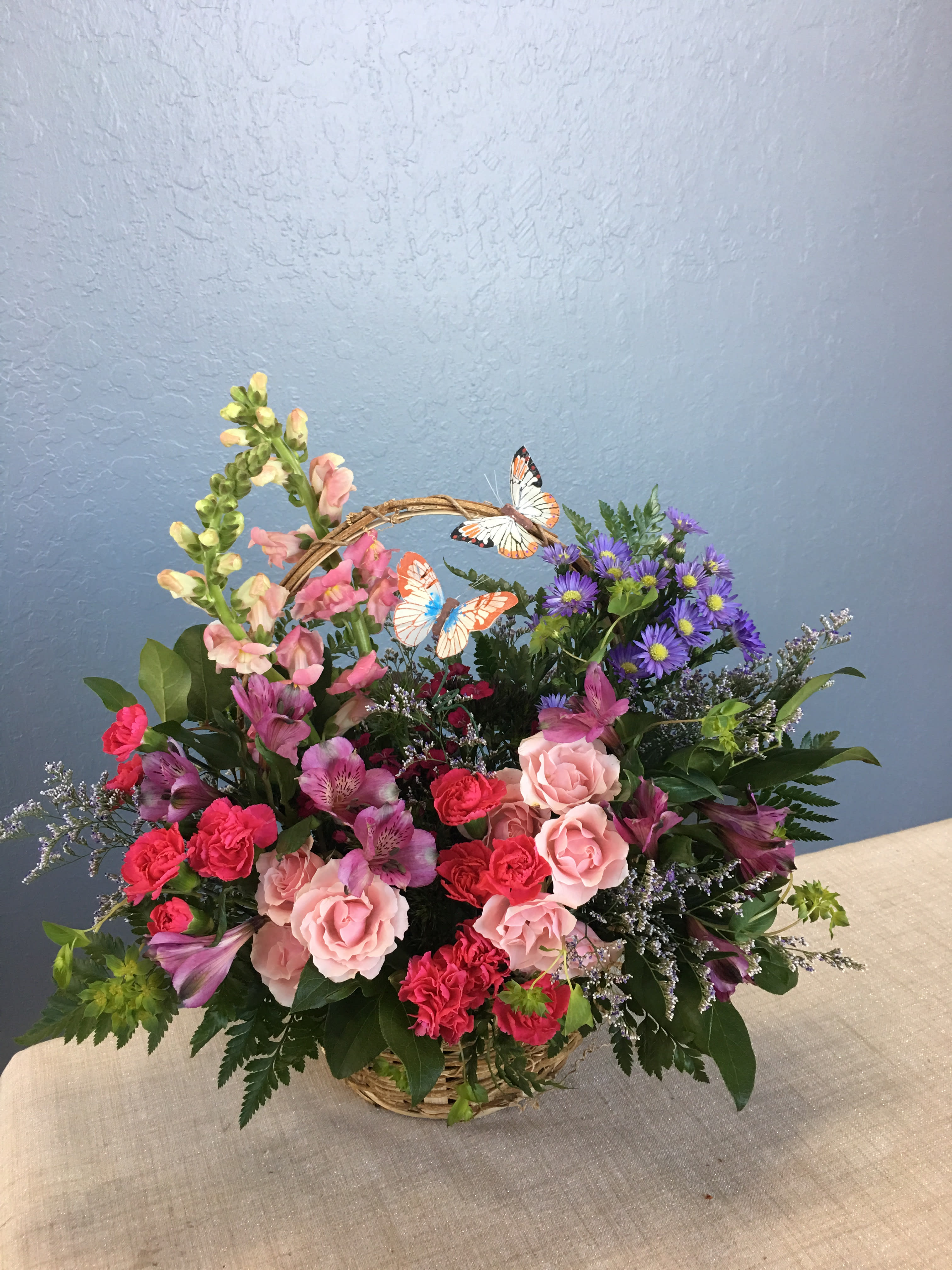 Basket arrangement of pink and purple flowers with butterfly picks