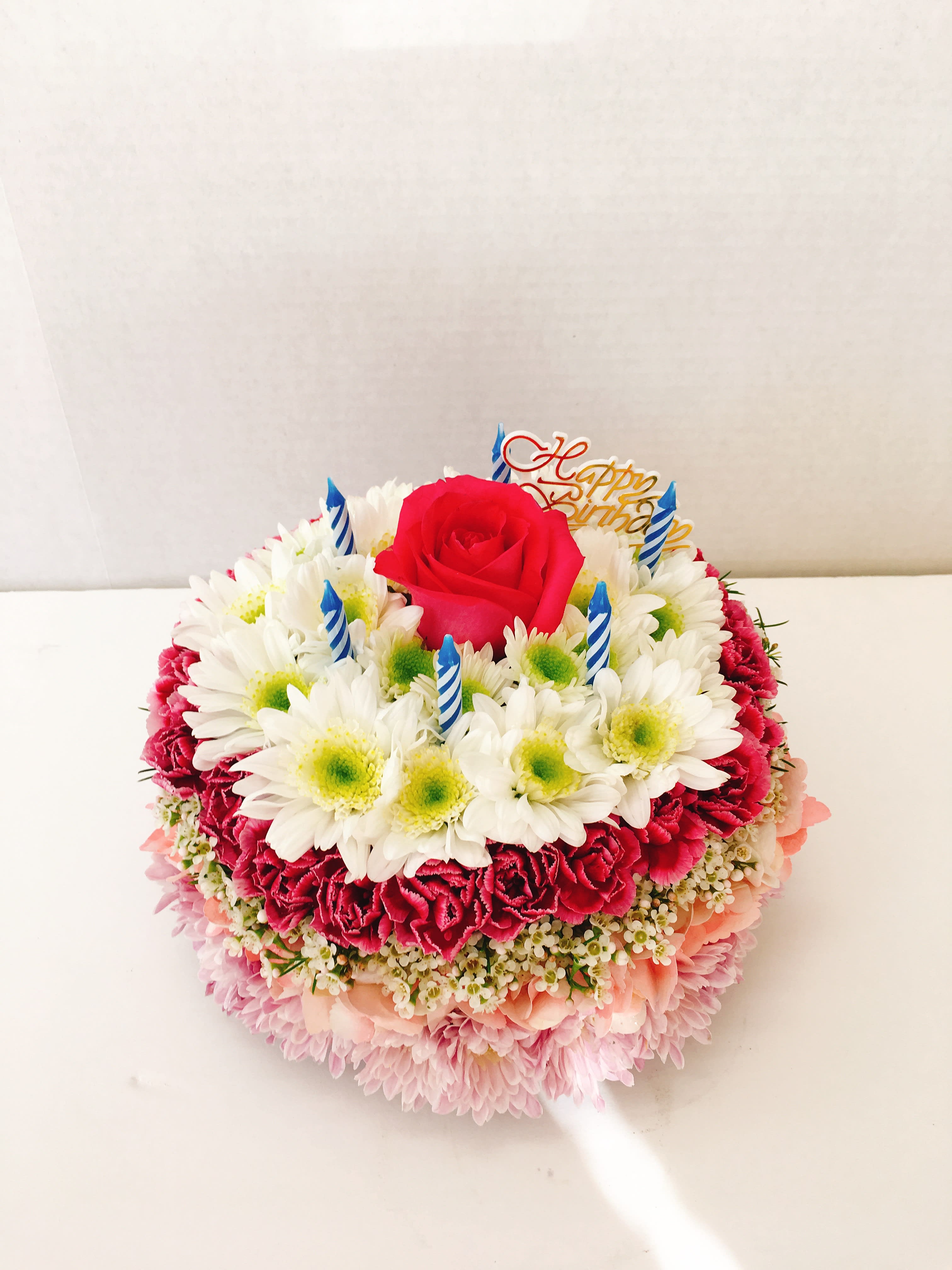 Round birthday cake made of flowers with a red rose and candles