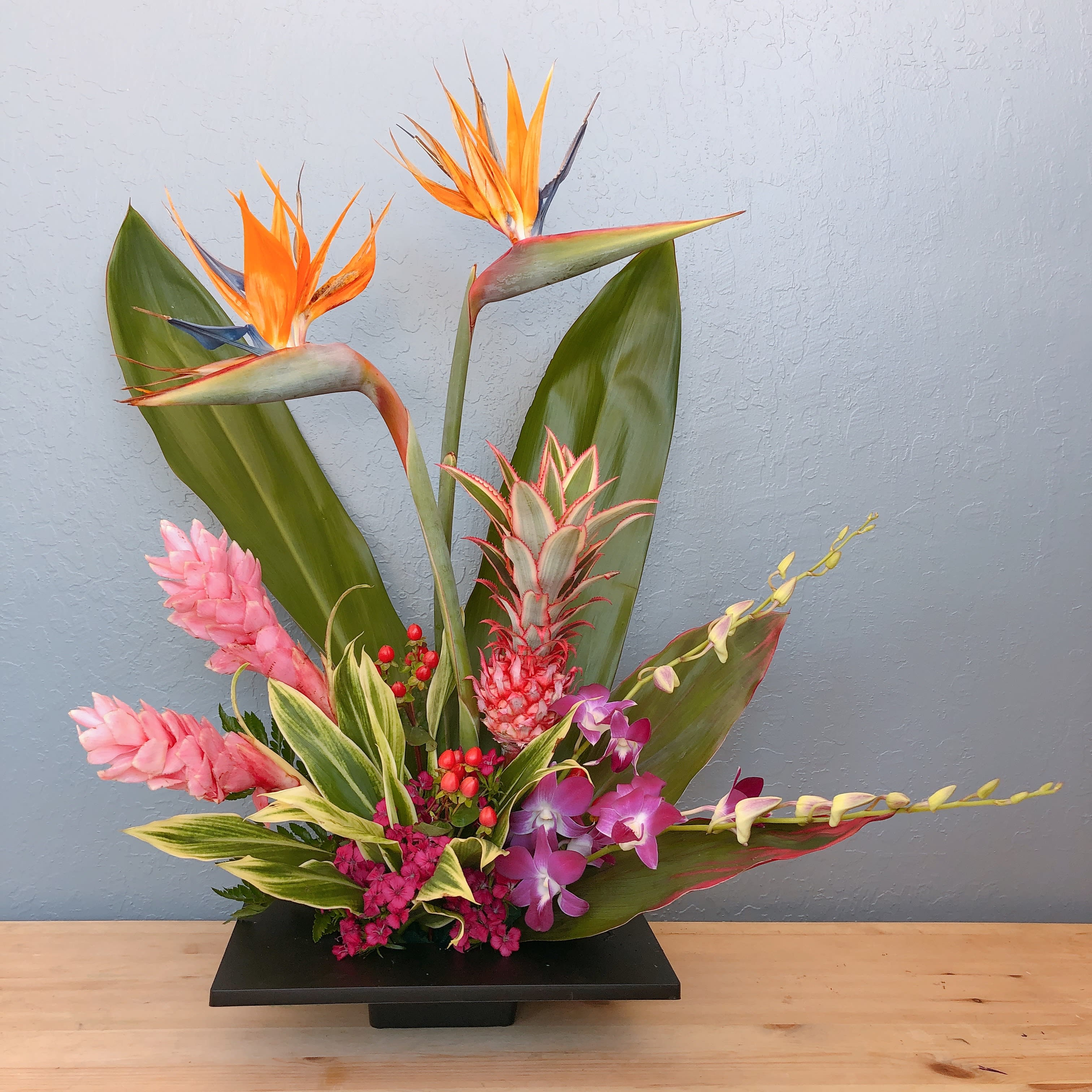 Tropical floral arrangement with orange bird-of-paradise and pink orchids in a black vase