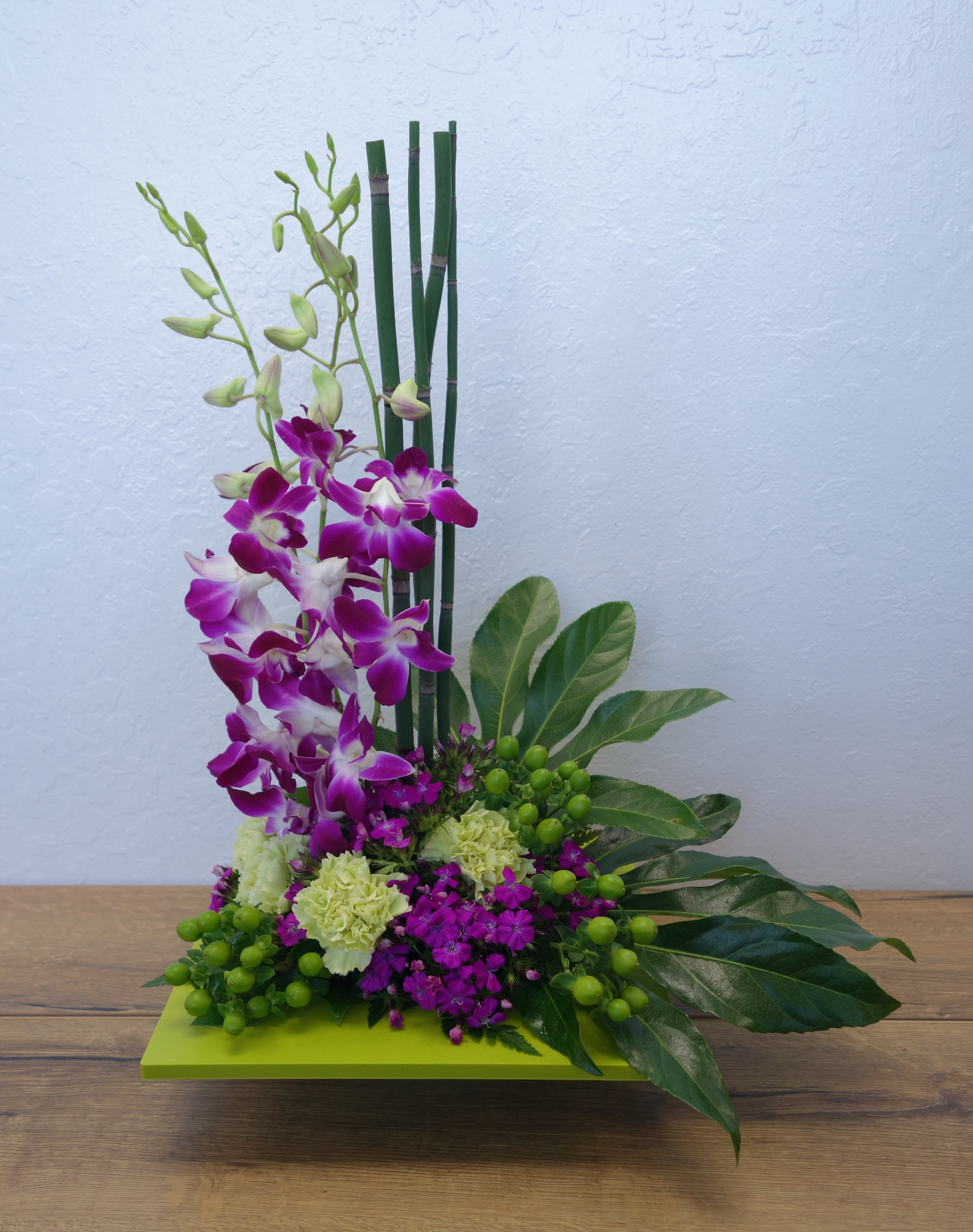 Zen Artistry - Purple dendrobium orchids, green carnations, dark pink Sweet William, an emerald palm leaf and other tropical greens are arranged in a square kiwi-colored container. Perfect when you've got a yen to send Zen! Approximately 12 1/4" W x 23" H. T81-1A 