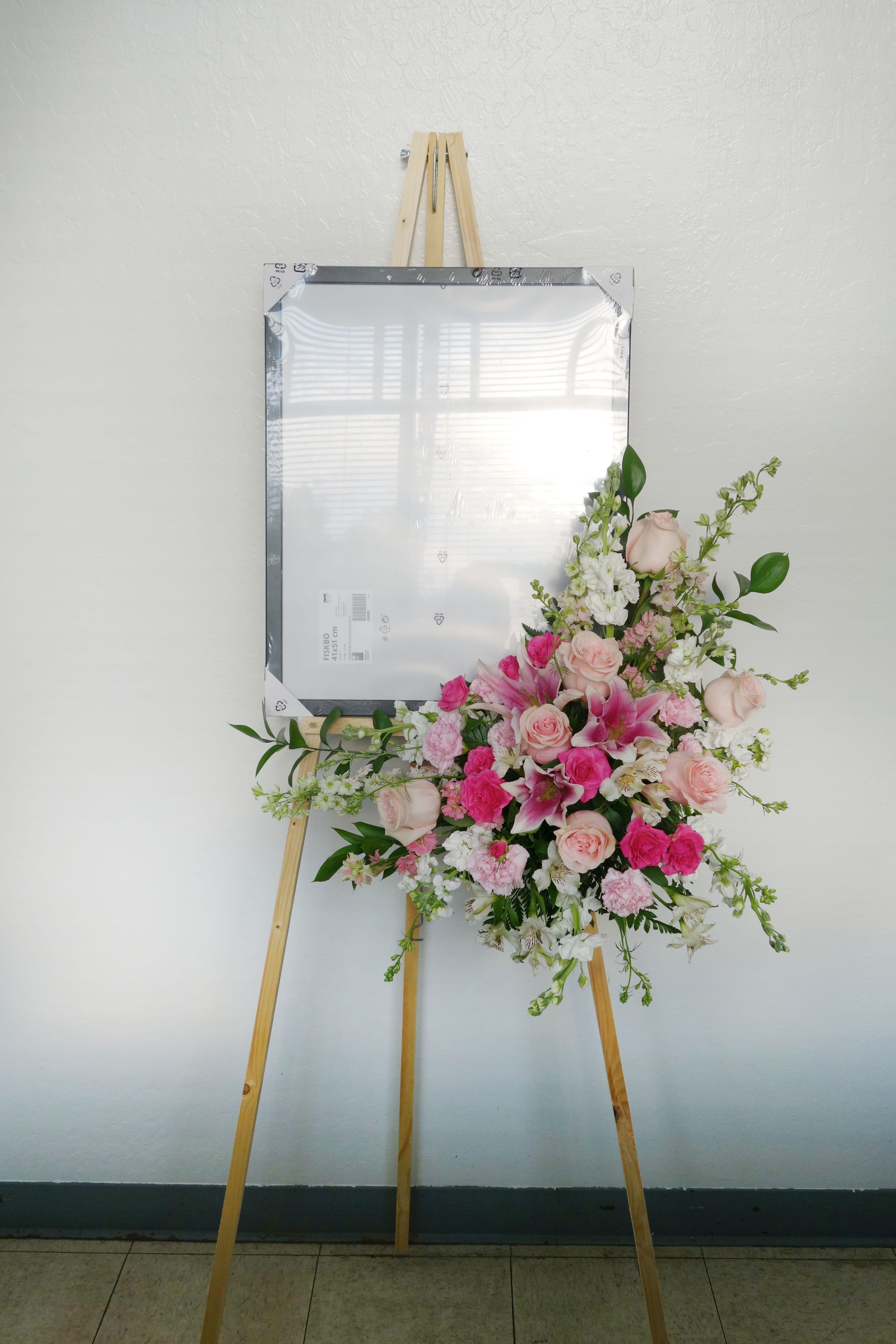 Pink and white floral spray on a wooden easel with a framed sign