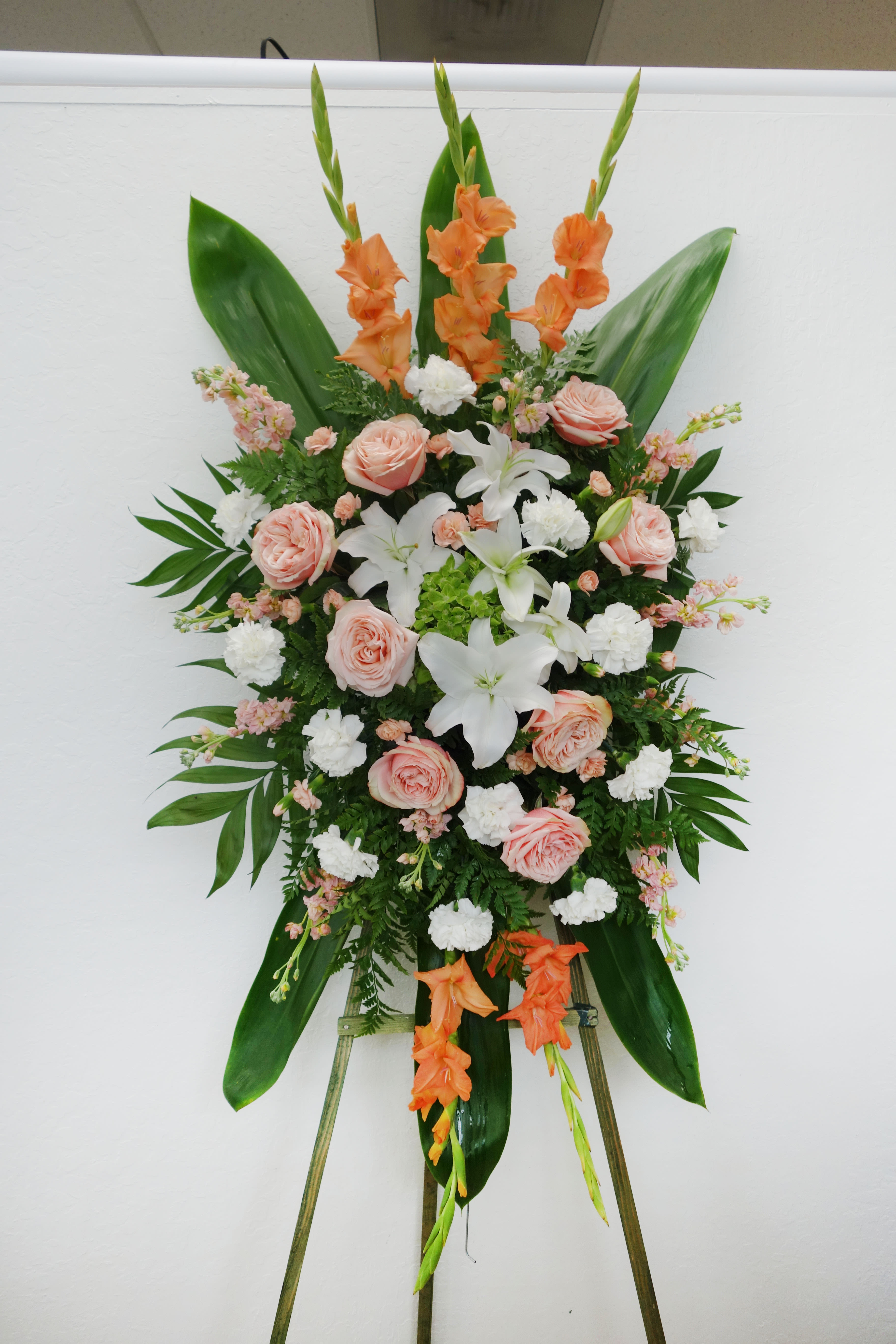 Standing floral spray with peach roses, white lilies, and orange gladiolus