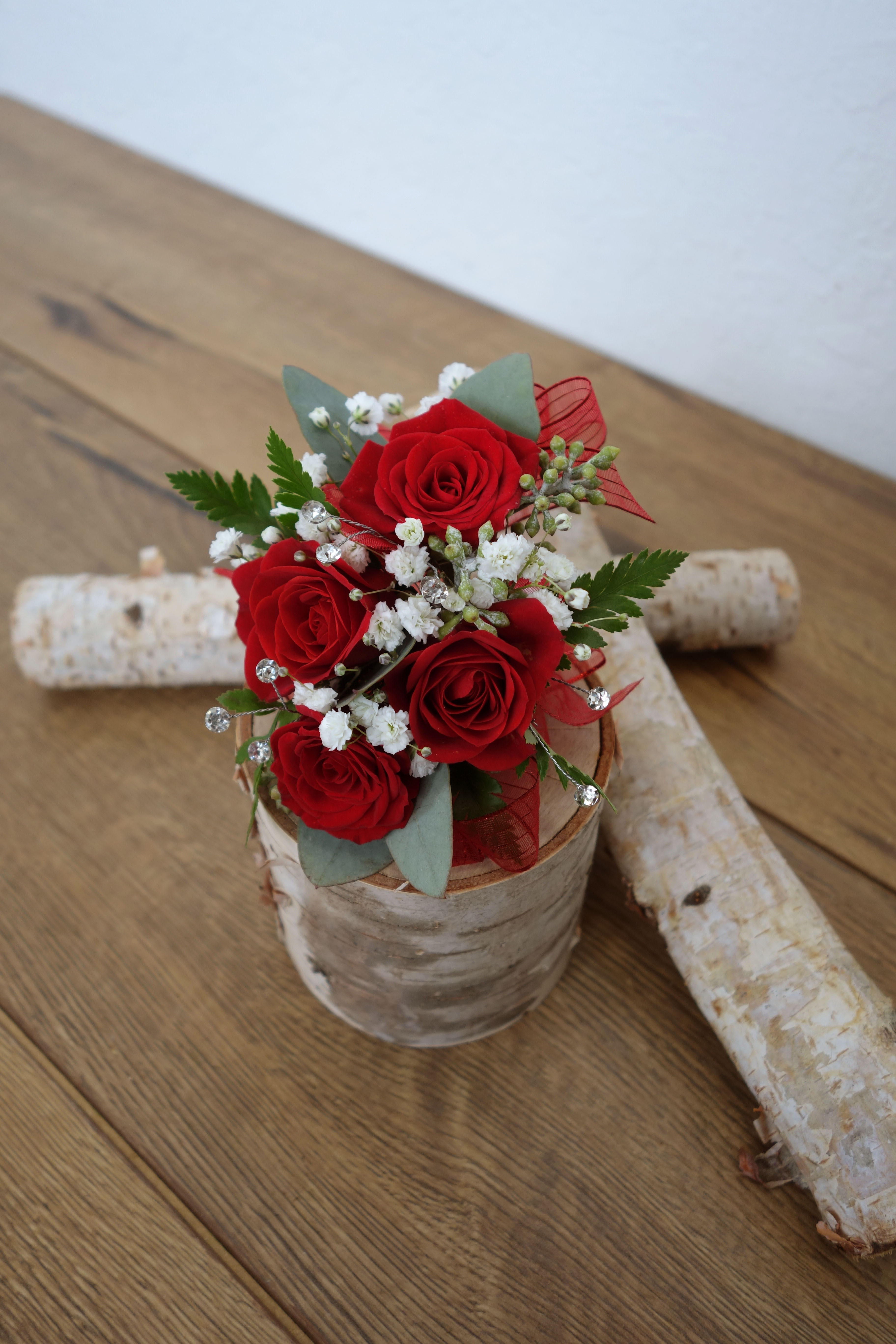 Small bouquet of red roses with white filler flowers in a rustic container