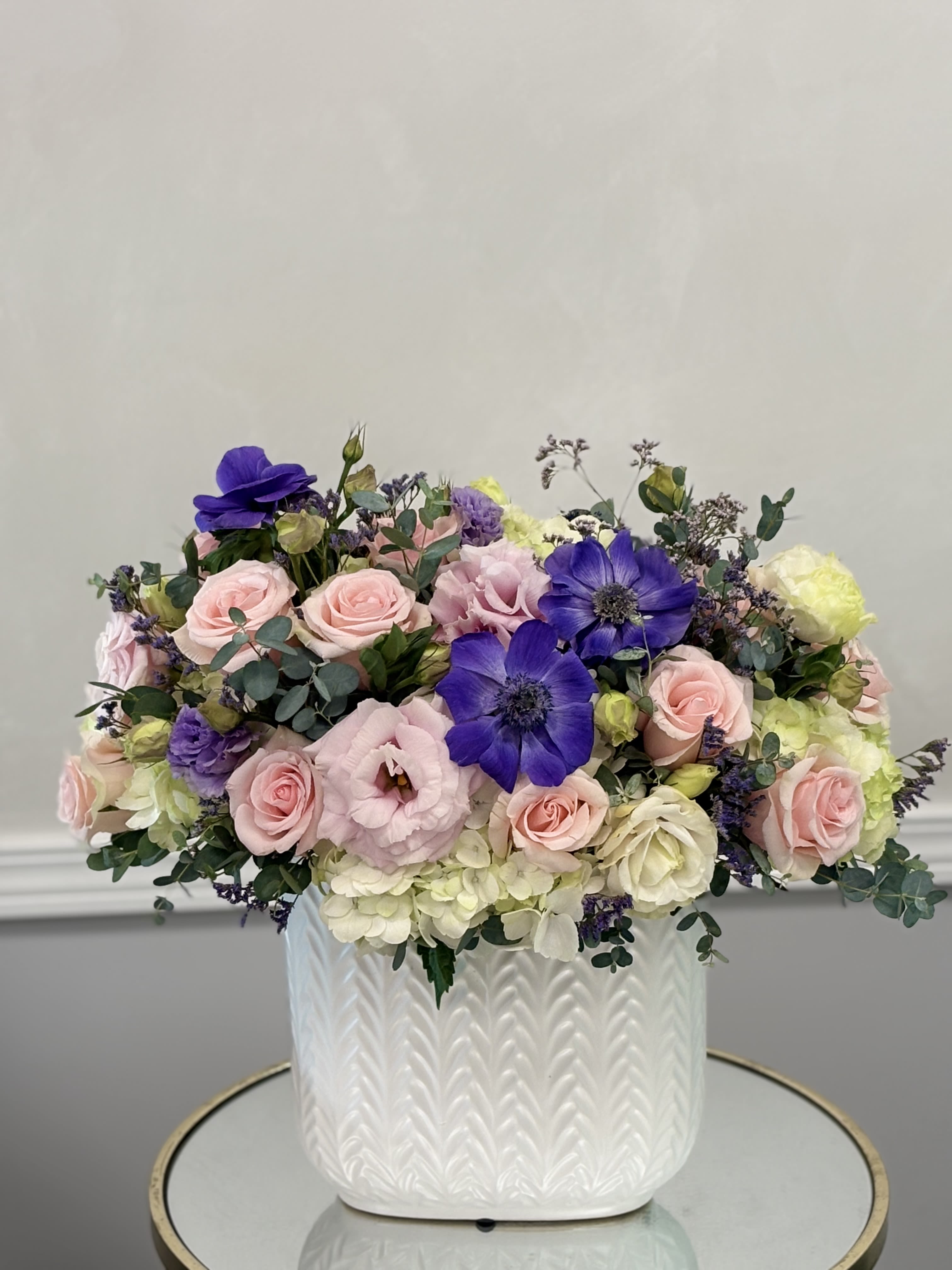 Mixed pink and purple flowers arranged in a white textured vase