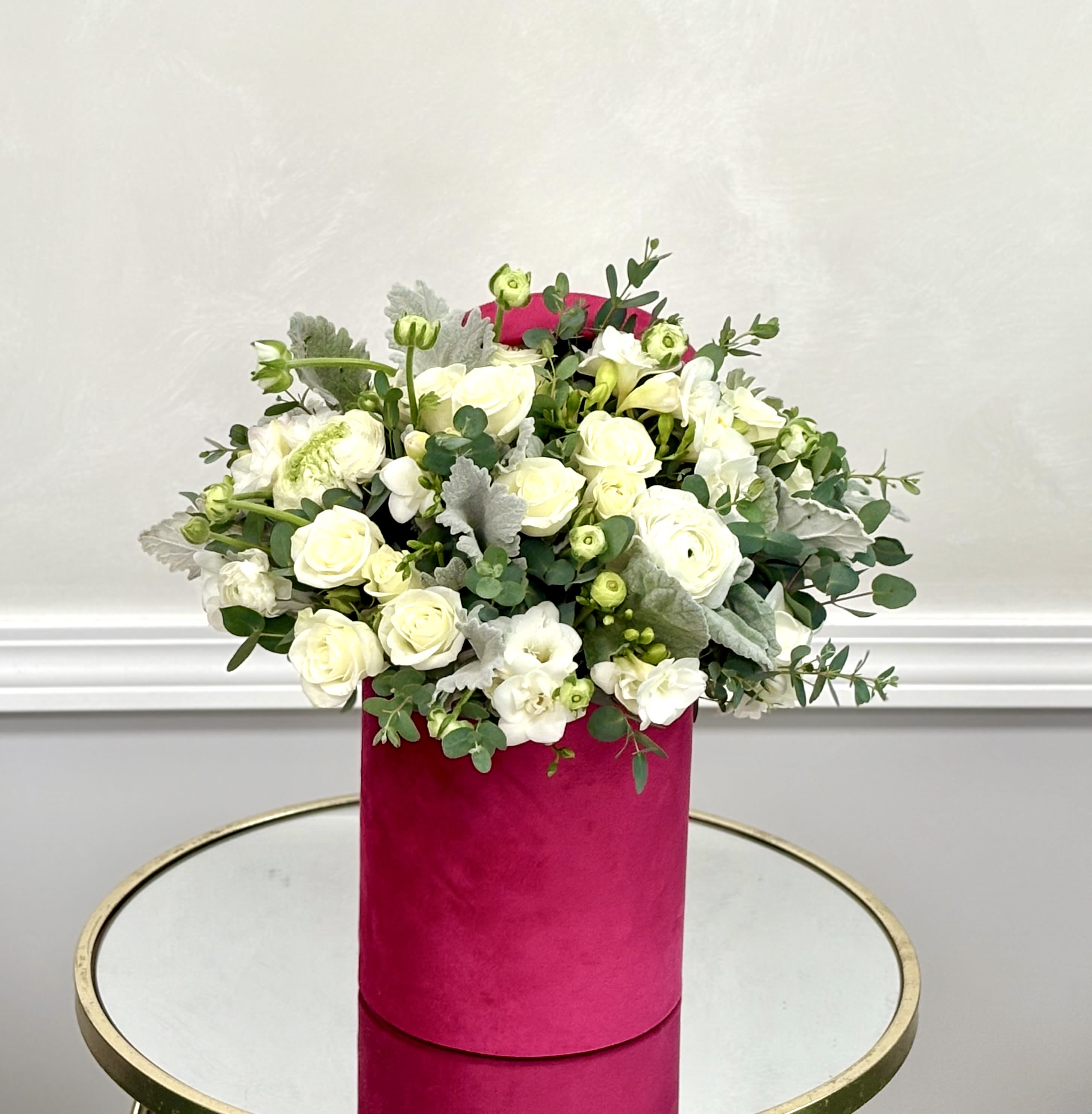 White roses and small white blooms in a pink cylindrical box
