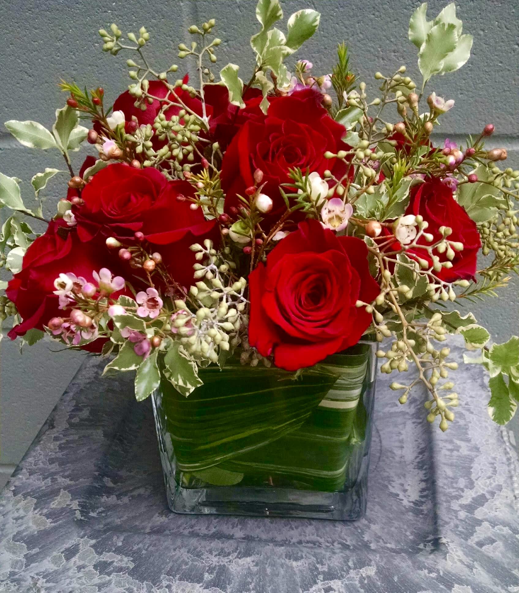 Red rose arrangement with pink filler blooms in a leaf-wrapped glass cube vase