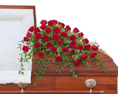 Red rose casket spray with trailing greenery on a wooden casket