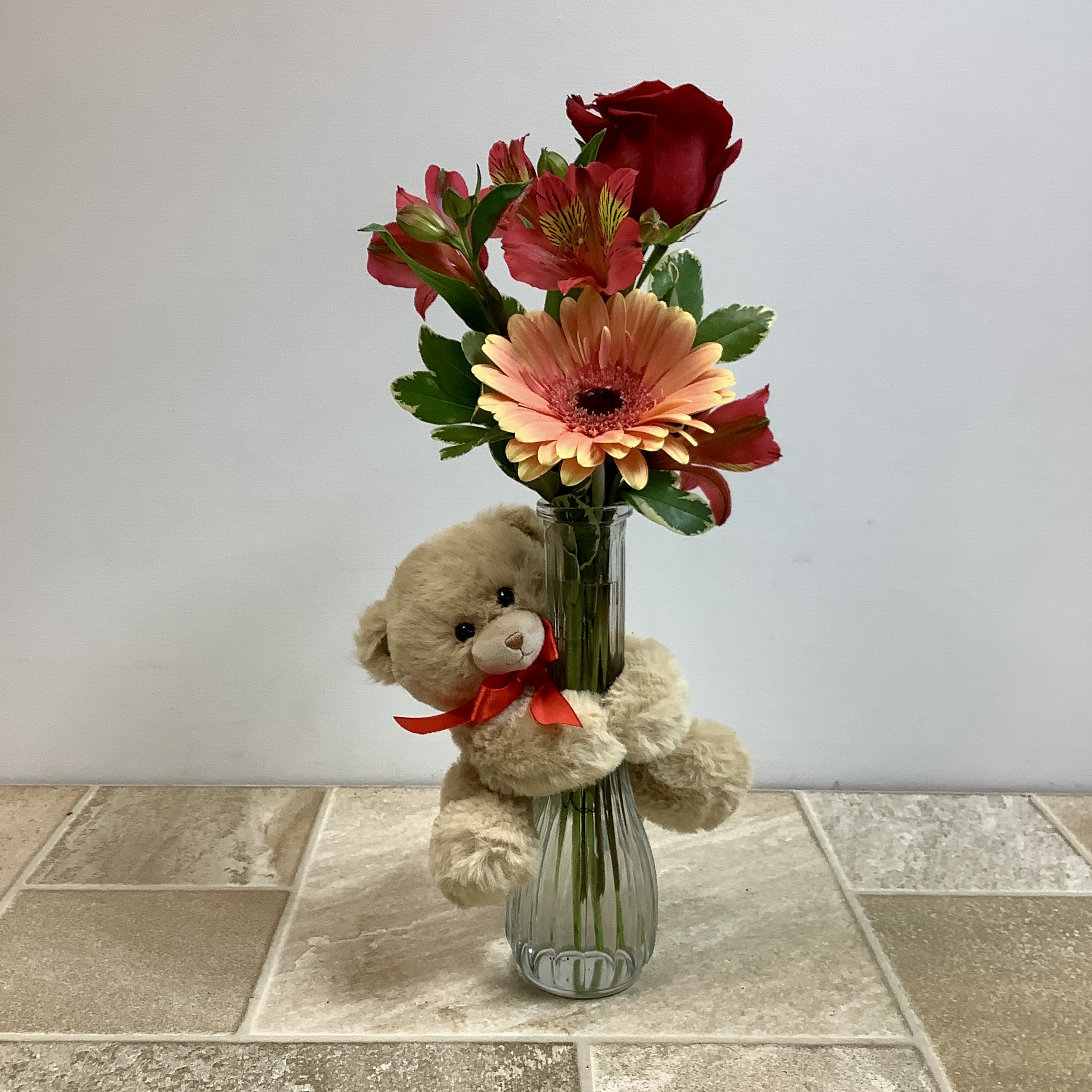 Teddy bear beside a vase of red and peach flowers