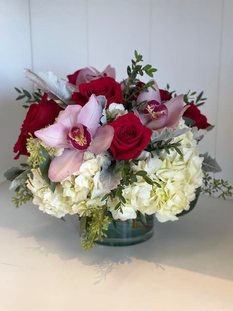 Bouquet of red roses, pink orchids, and white hydrangeas in a glass vase