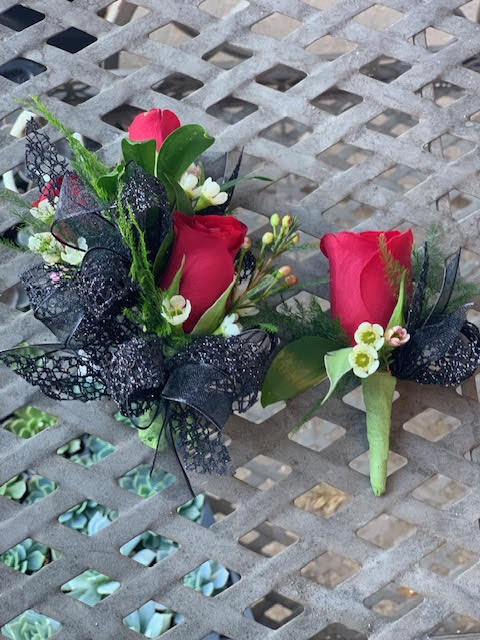 Two red rose boutonnieres with black ribbon accents on a metal table