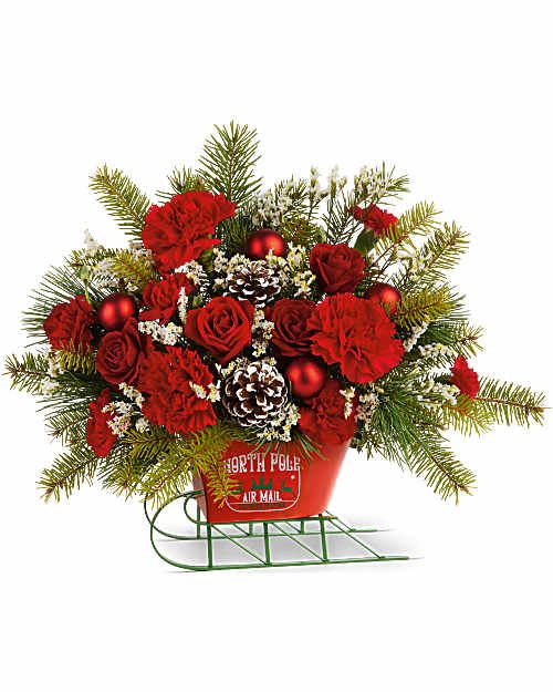 Teleflora's Sleigh All The Way Bouquet - Teleflora's Sleigh All The Way Bouquet delivers bold holiday color with a playful twist! Red blooms, winter greens, and festive accents are hand-arranged in Teleflora's North Pole Sleigh Keepsake. This Christmas arrangement brings cheerful style and seasonal spirit to any celebration.