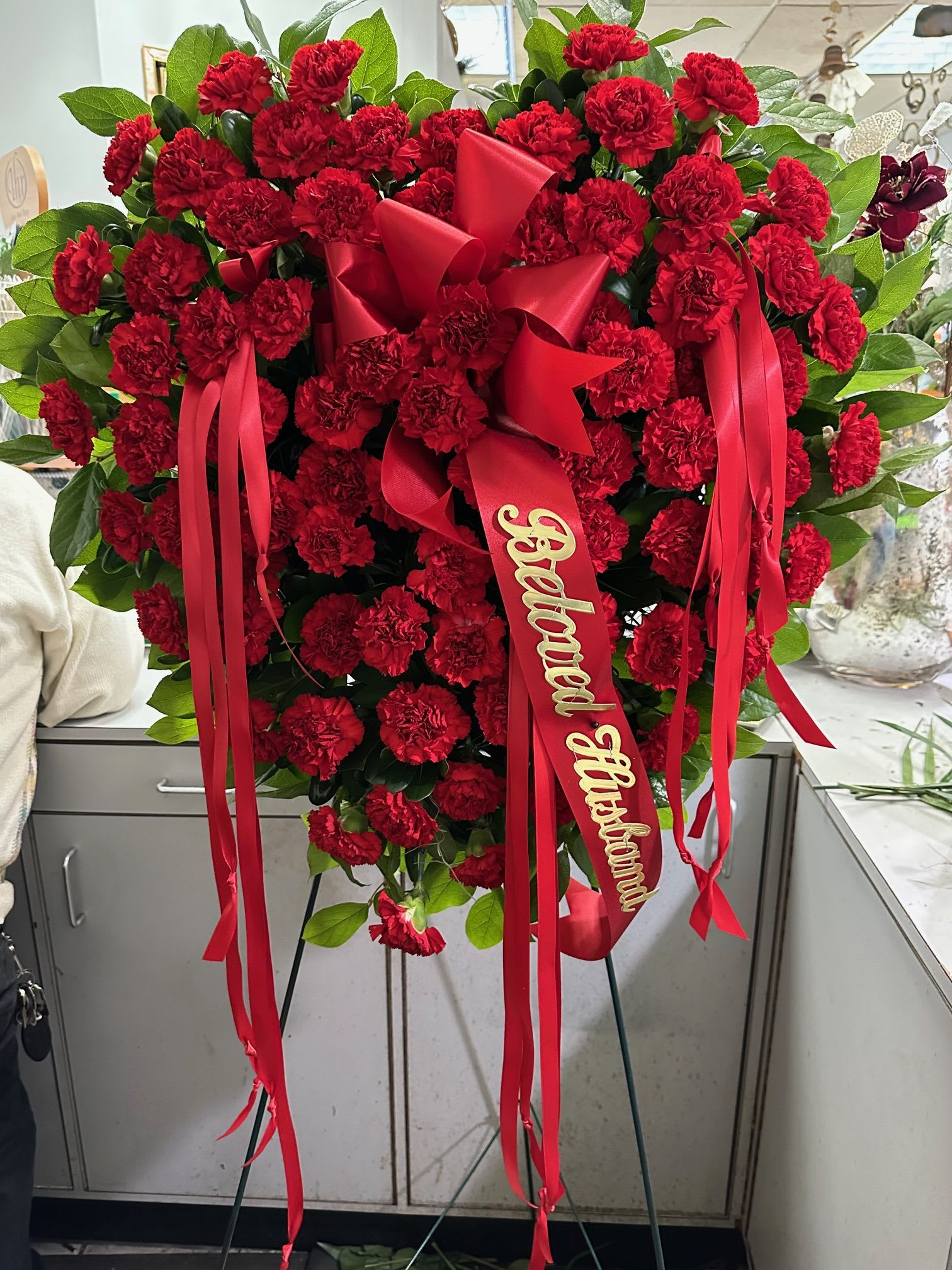 Heart-shaped standing spray of red carnations with ribbon