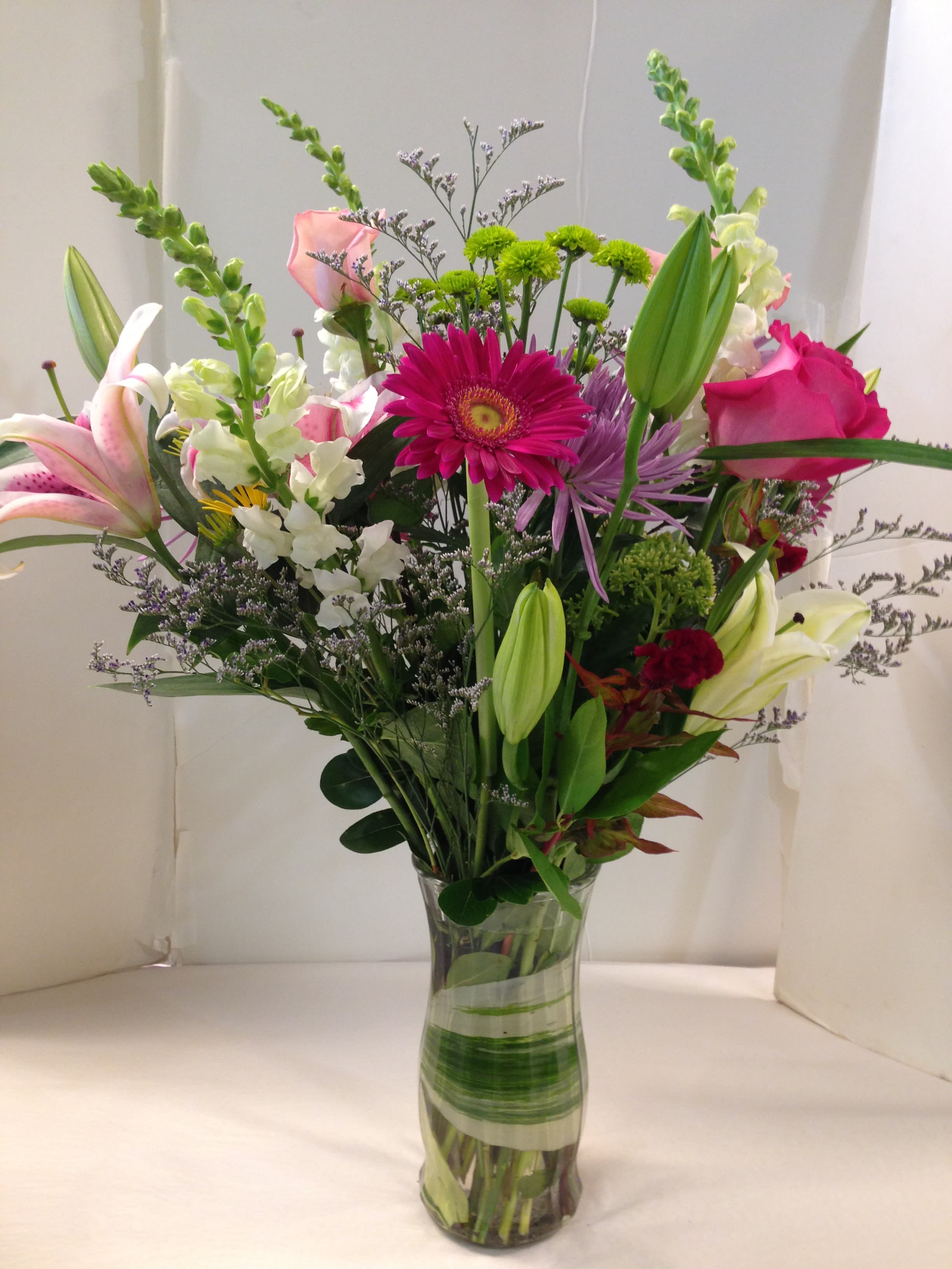 Mixed bouquet of lilies, roses, and daisies in a clear glass vase