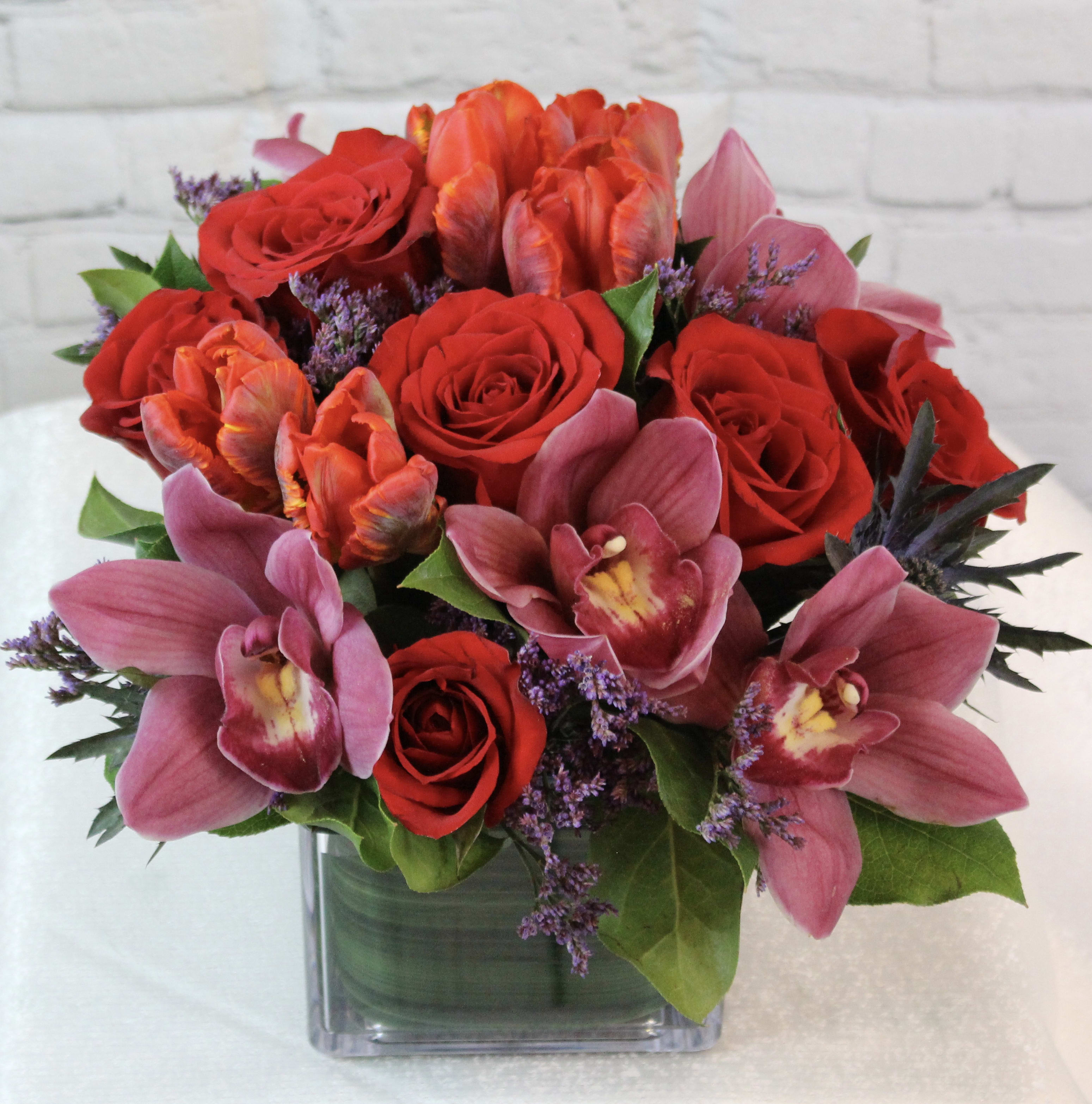 Bouquet of red roses and pink orchids in a square glass vase