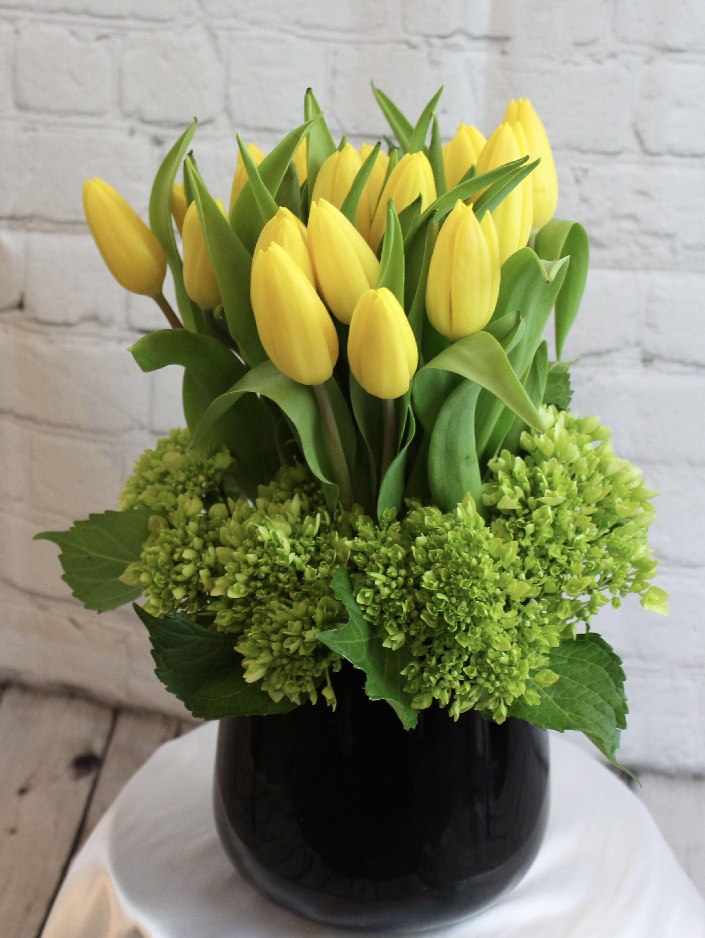 Yellow tulips arranged in a black vase with green hydrangeas
